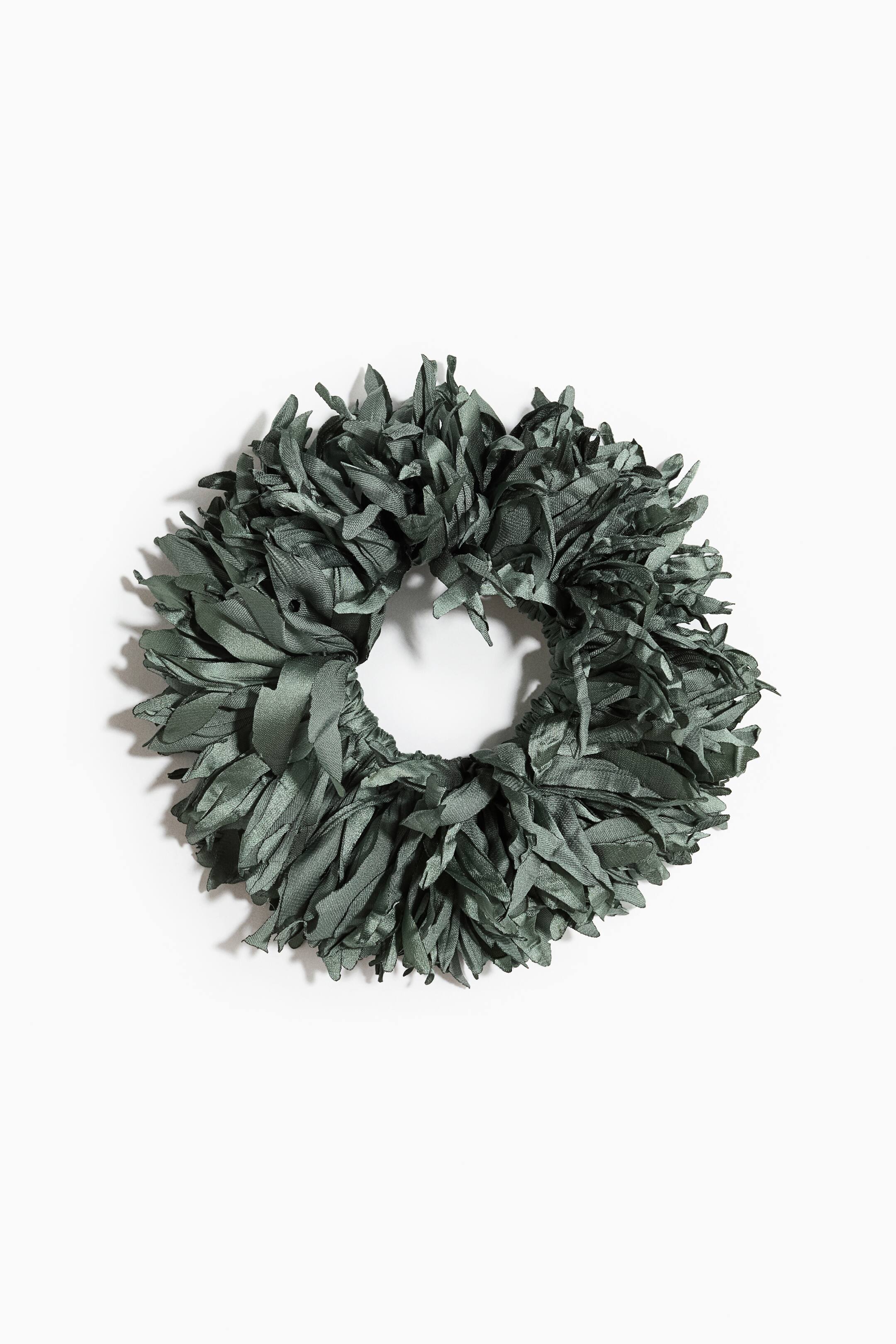 Zobacz większy obraz: Ciemnozielona gumka scrunchie prezentuje obszerny, inspirowany kwiatem design, stworzony z licznych wąskich, przypominających płatki pasków materiału o delikatnym połysku. Teksturowane paski promieniście rozchodzą się od centralnej elastycznej opaski, tworząc pełny, falowany wygląd.