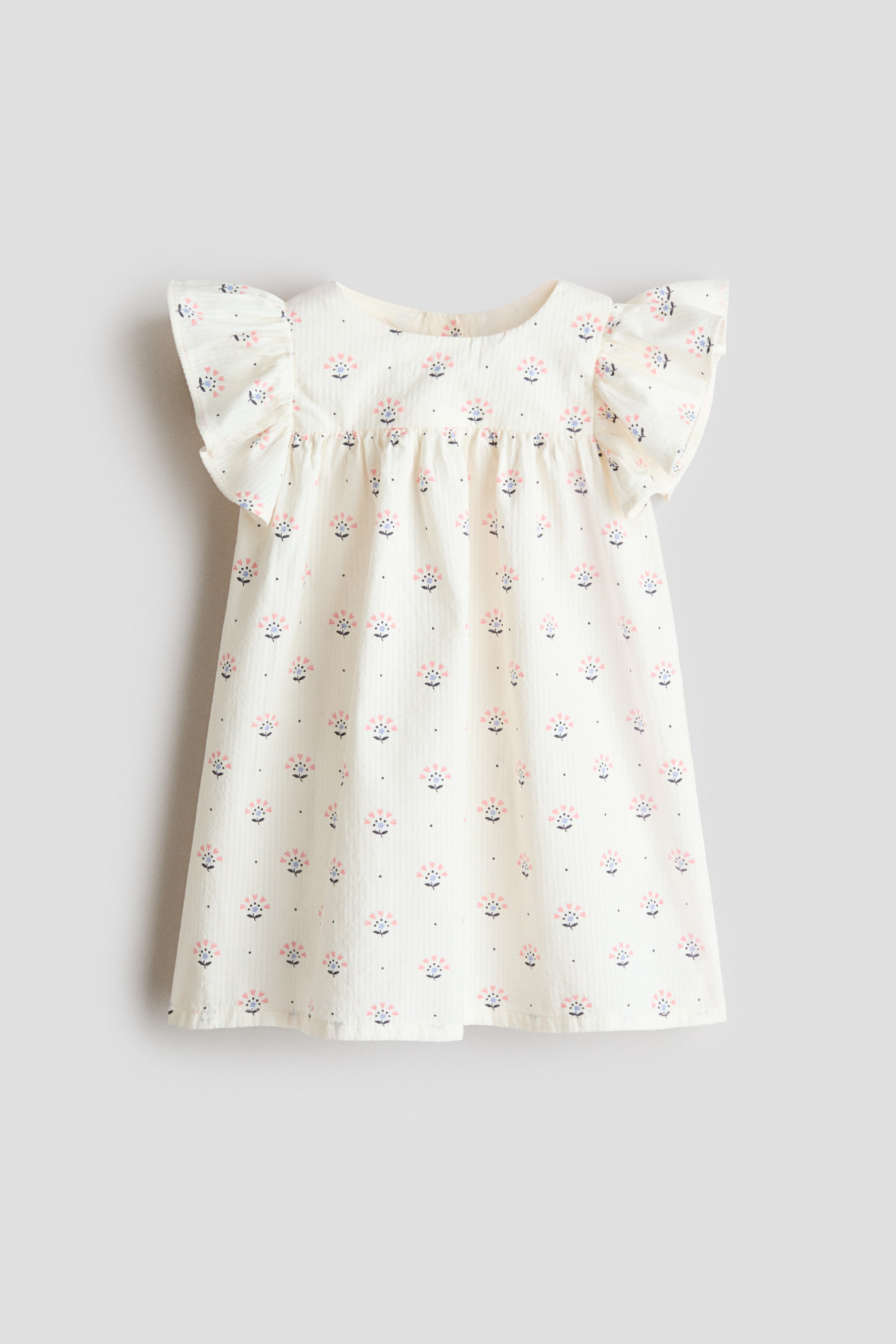 View larger image: The dress showcases its front view. This off-white attire highlights subtle vertical stripes, a recurring floral motif in pink, light blue, and dark blue dots, a round neckline, short ruffled sleeves, and a gathered bodice that transitions into a relaxed A-line silhouette.
