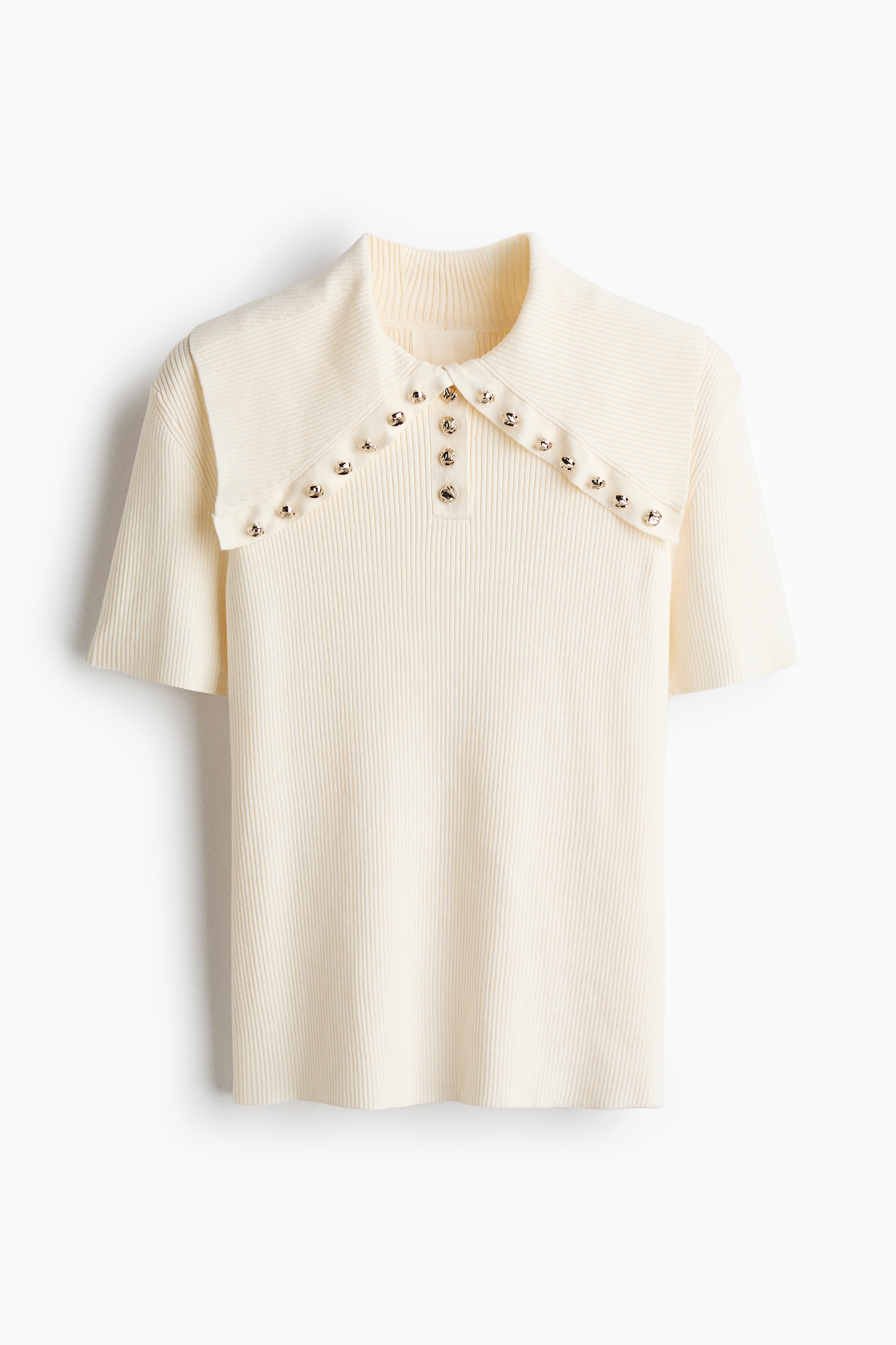 A cream-colored, fitted, rib-knit top is being worn by the model, featuring short sleeves, a central button placket, and a large collar lined with decorative gold buttons.