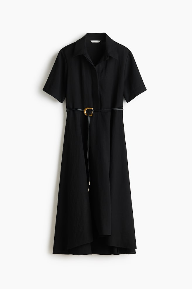 Une robe chemise noire se présente de face, confectionnée dans un tissu texturé et dotée d'un col pointu, d'une patte de boutonnage sur le devant et de manches courtes. Une fine ceinture noire avec une boucle en forme de C dorée serre la taille, et la jupe évasée tombe sur un ourlet asymétrique. - 1