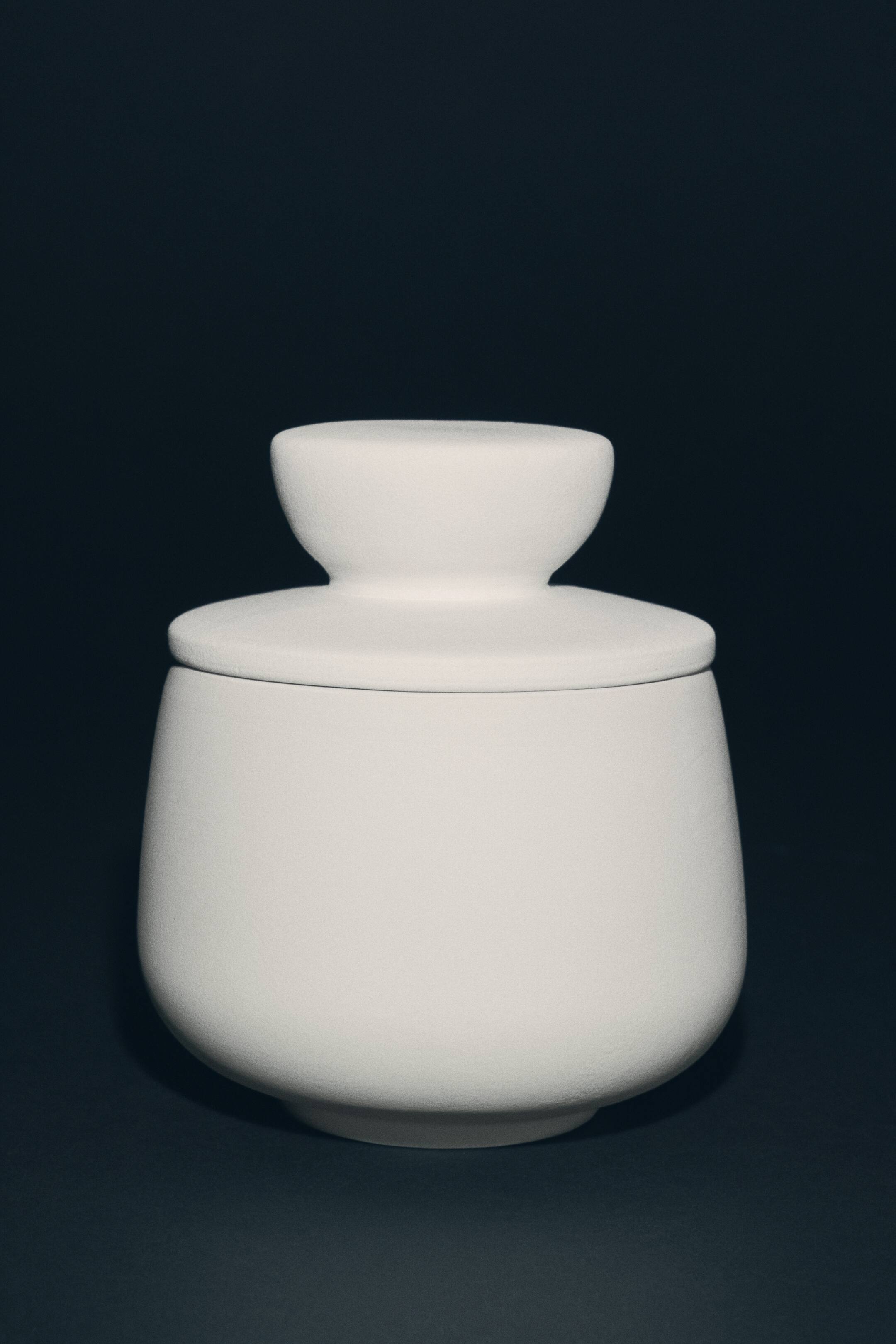 View larger image: A white lidded stoneware pot is shown from the front, featuring a rounded body with a textured matte finish. The matching lid rests on top, showcasing a distinctive, wide pedestal-shaped knob.