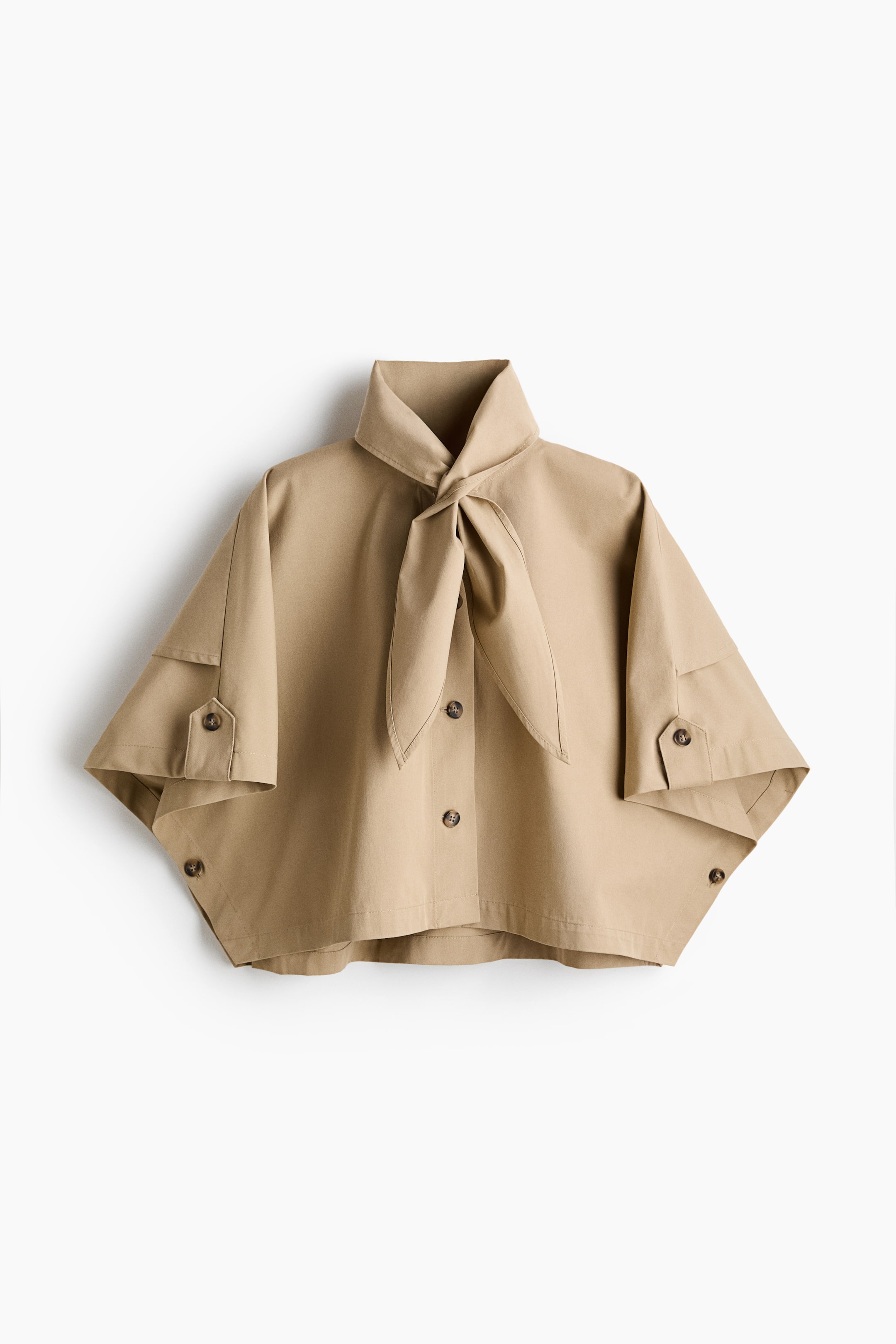 View larger image: A beige cropped blouse featuring a stand collar with a front tie knot. Designed with a button-front closure, wide short sleeves with buttoned tabs, and visible side buttons near the hem.