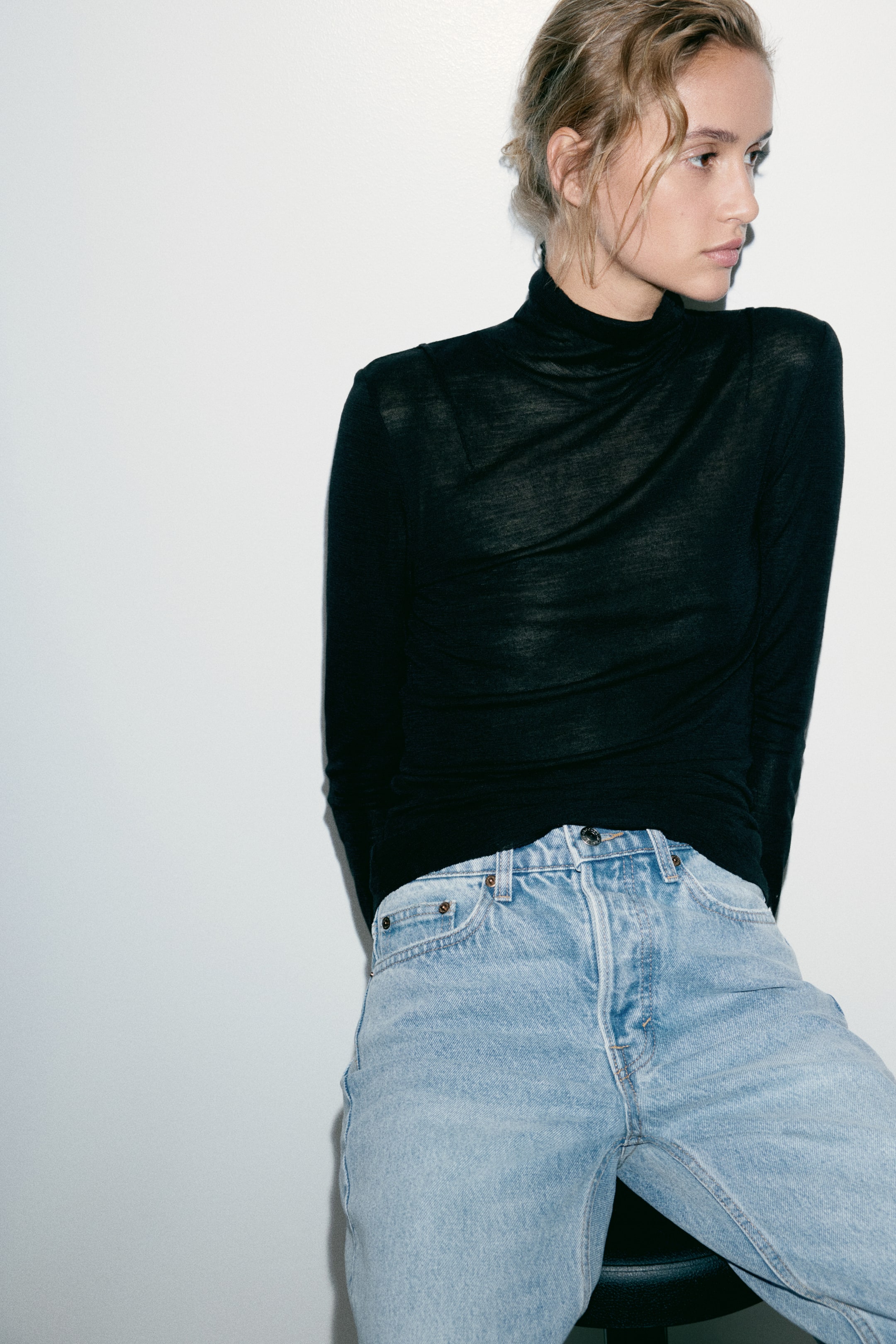 View larger image: The model is wearing light blue, high-waisted denim jeans styled with a long-sleeved black turtleneck top. The jeans feature a classic five-pocket design, belt loops, and a button closure at the waist.