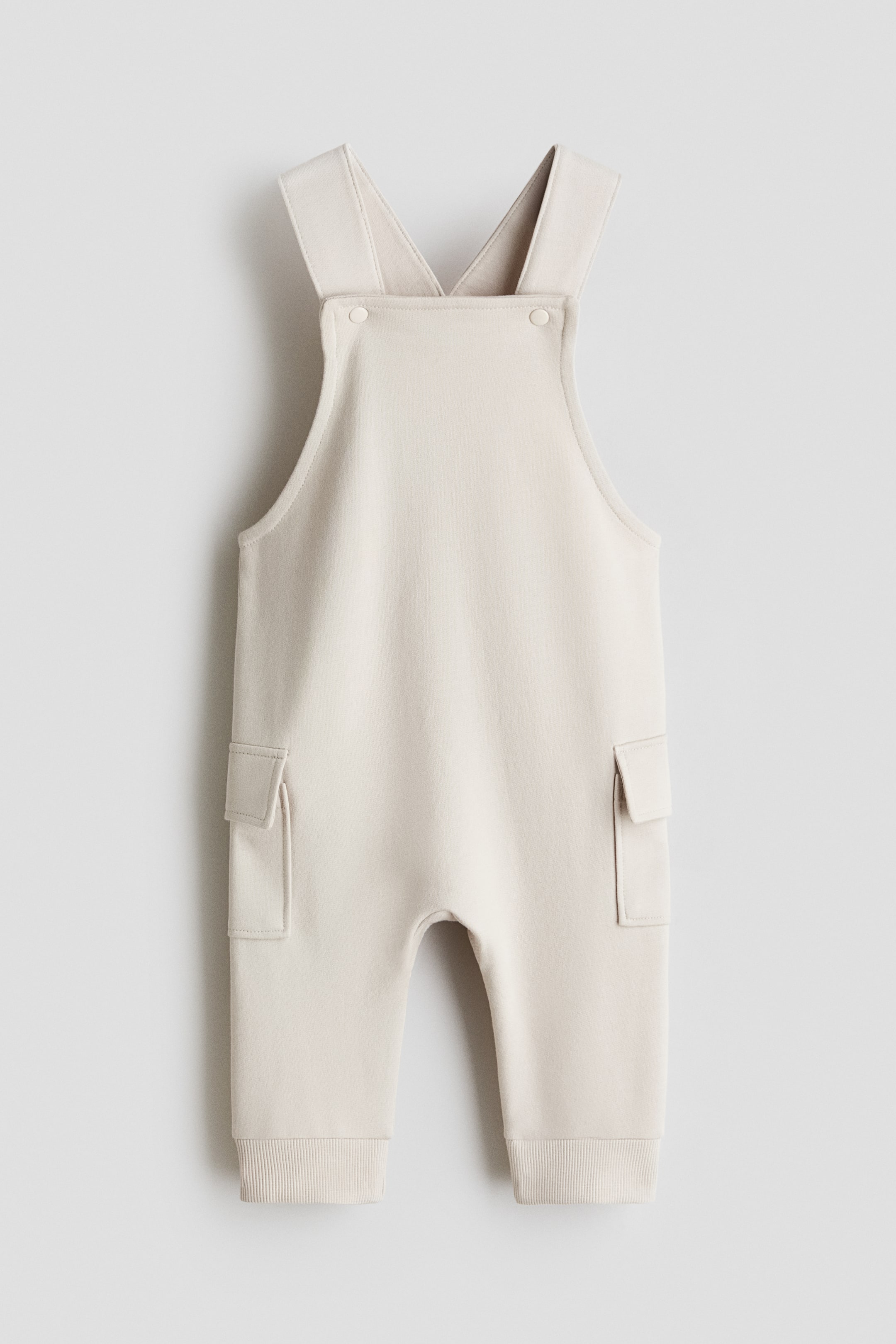 Ver imagen más grande: Peto beige claro, confeccionado en tejido de sudadera, presentado de frente. Presenta tirantes anchos con cierres a presión ajustables en el peto, dos bolsillos aplicados en las piernas y puños acanalados en los bajos.