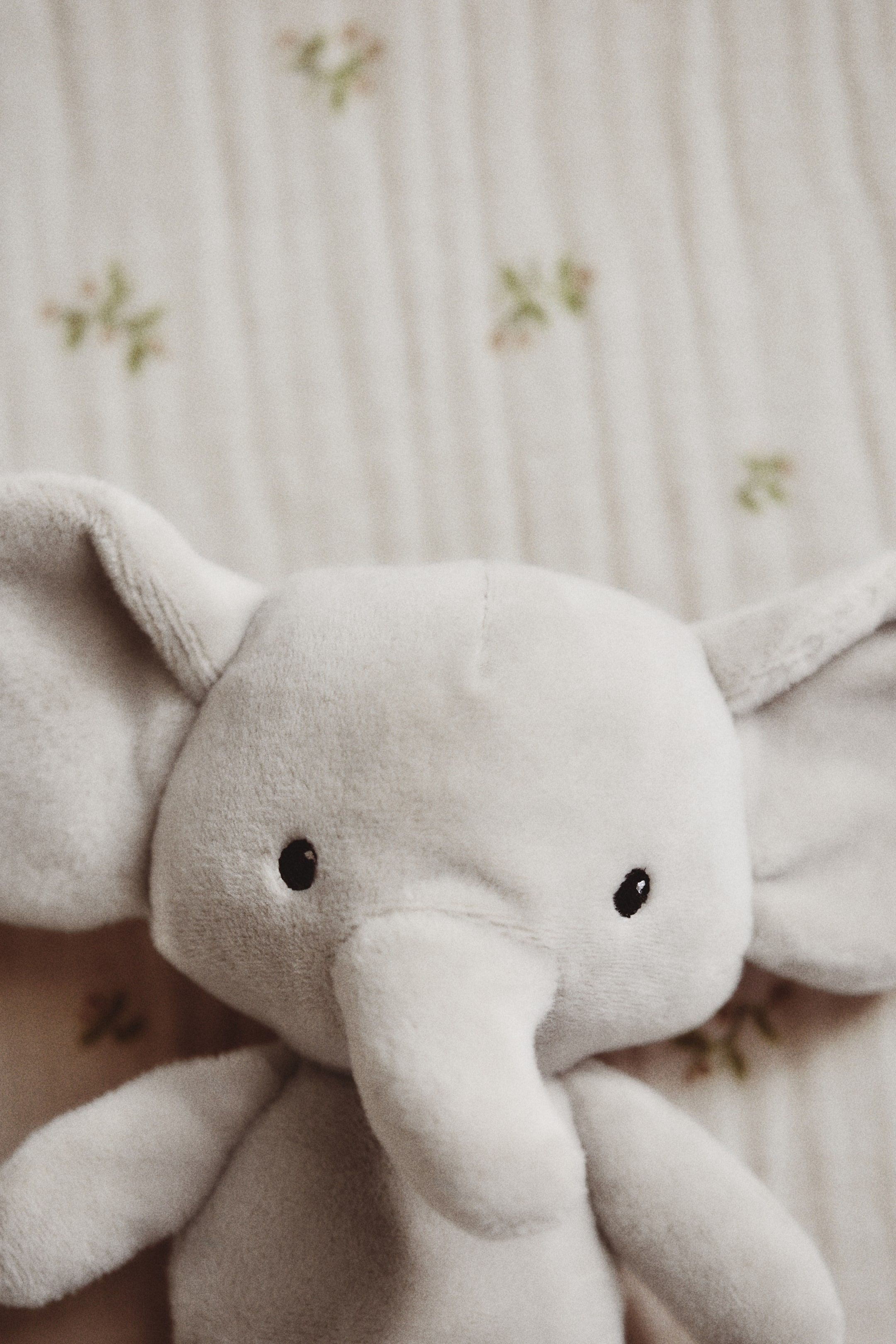 View larger image: An elephant-shaped padded baby rattle is facing front, crafted from light grey, soft pile fabric, and featuring large, round ears, small black embroidered eyes, and a short, curved trunk.