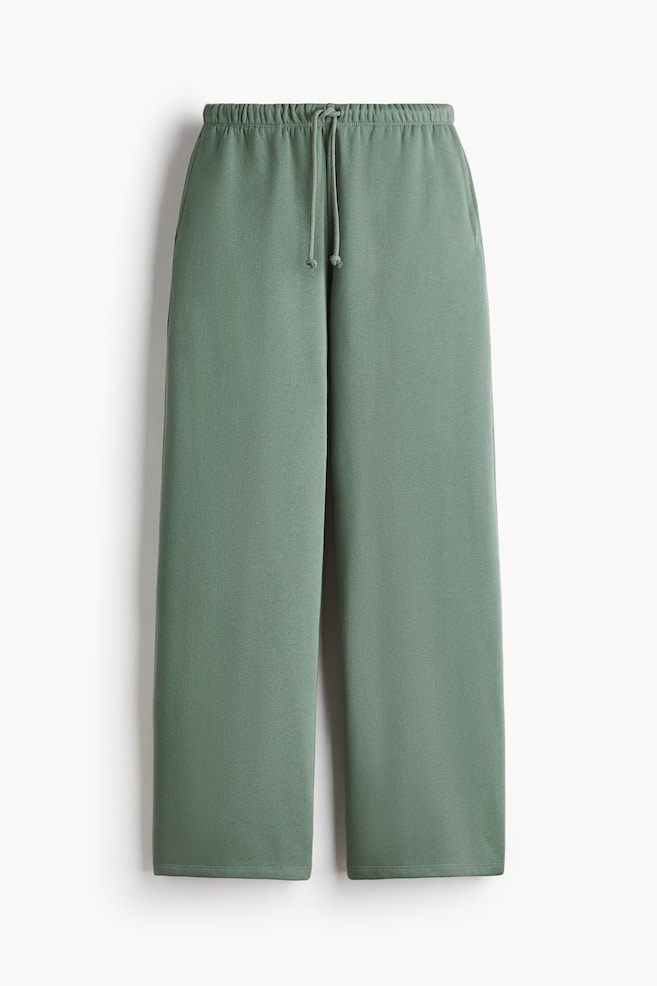A pair of green, loose-fit joggers is presenting from the front, featuring an elasticated, drawstring waist, discreet side seam pockets, and wide legs in a sweatshirt fabric. - 1