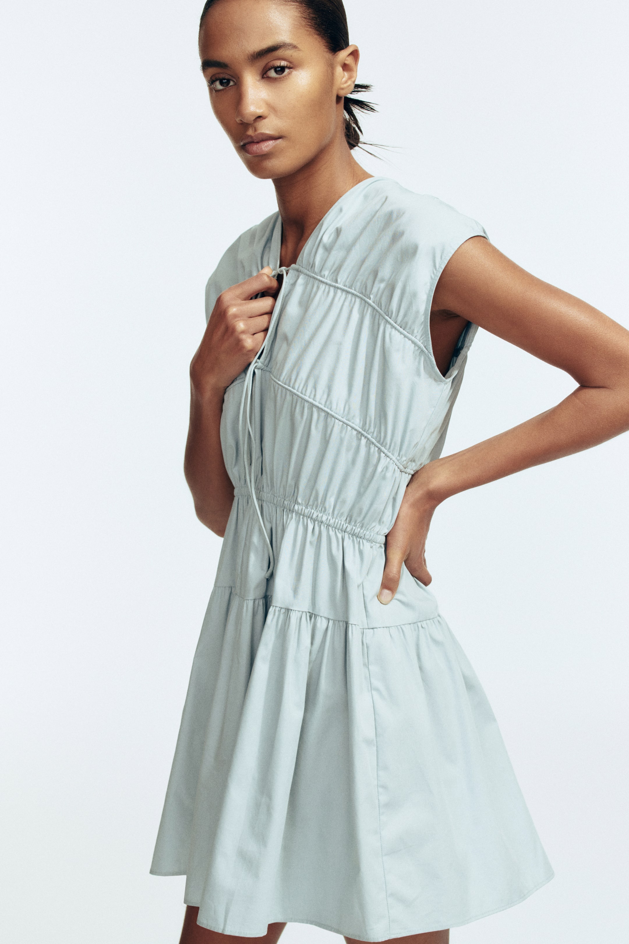 View larger image: A light blue sleeveless dress is featuring a V-neckline with a drawstring creating gathers across the bodice, an elasticated waist, and a tiered skirt, shown from the front.