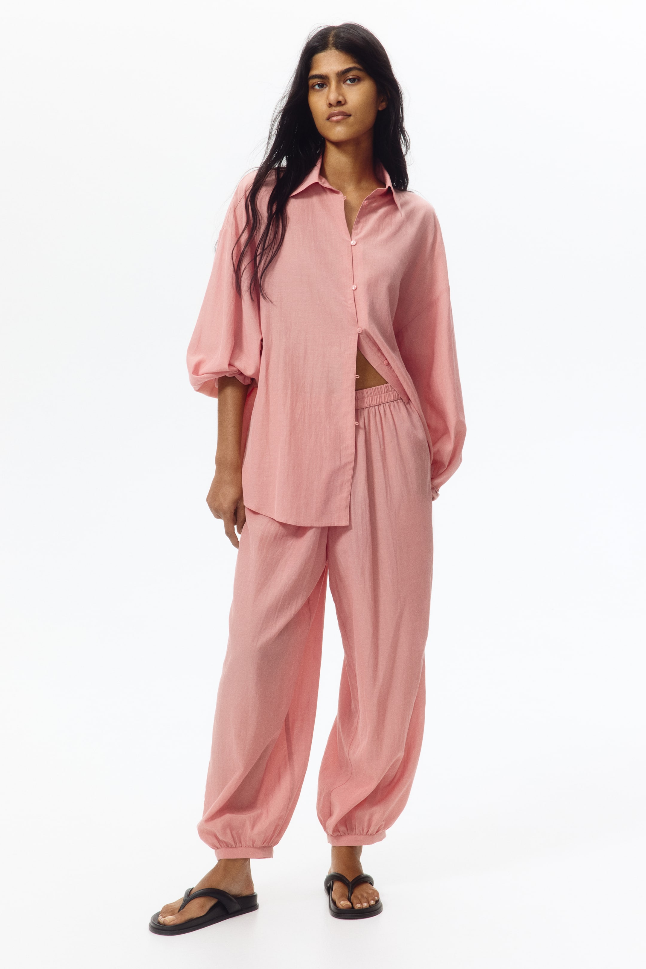 View larger image: Presenting a pink two-piece set, which includes a loose-fitting button-down shirt with a pointed collar and voluminous sleeves gathered at the cuffs, paired with matching wide-leg pants featuring an elasticated waistband and gathered ankles. The shirt is partially unbuttoned, revealing the pants' waistband.