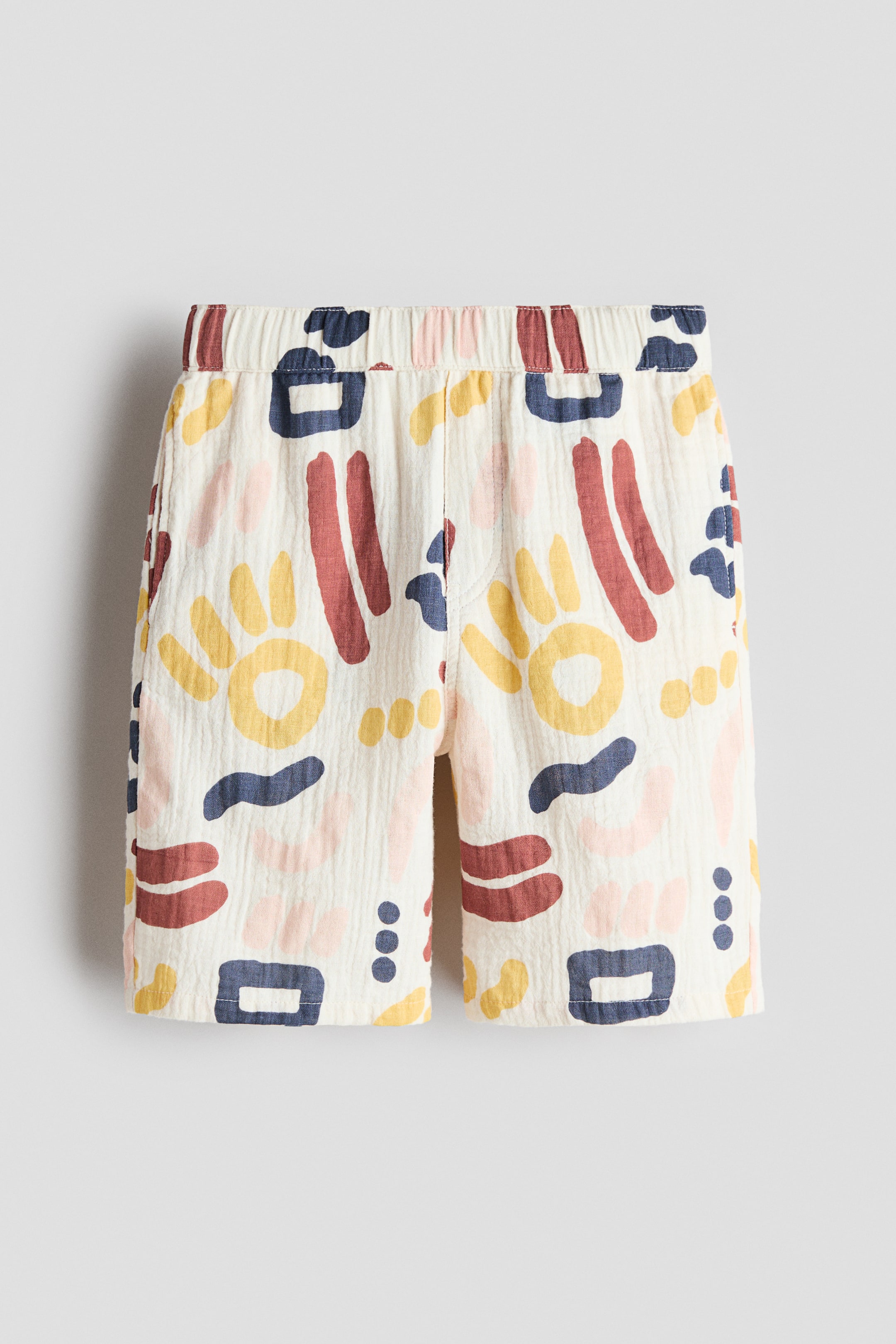 View larger image: Shorts, showcasing a frontal view, crafted from an off-white, crinkled fabric, featuring an abstract motif of reddish-brown, dark blue, yellow, and light pink shapes. They come with an elasticated waistband and two visible side pockets.