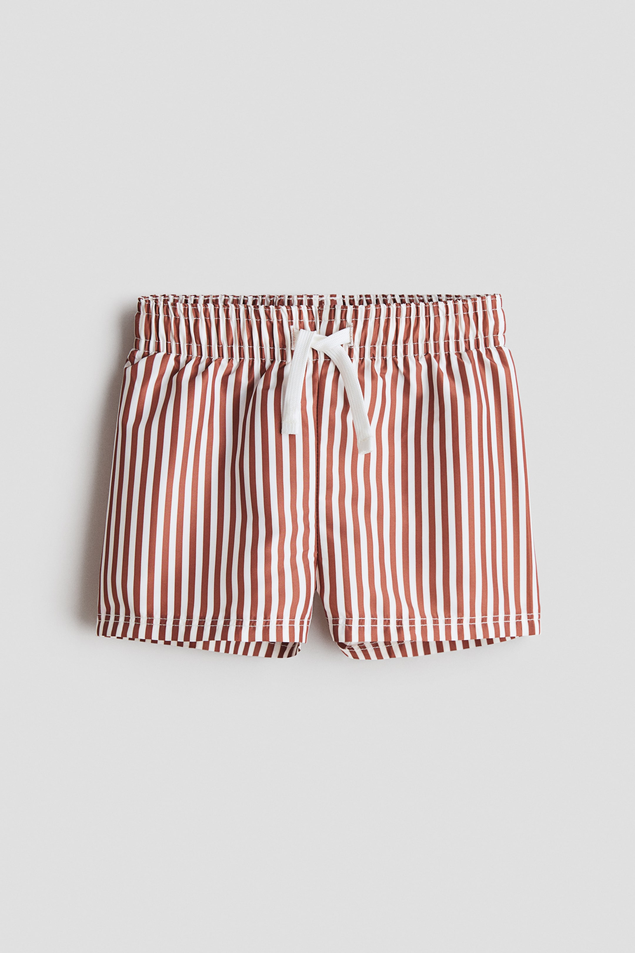 View larger image: The swim shorts, shown from the front, feature vertical brown and white stripes and an elastic waistband with a white drawstring tied in a bow.