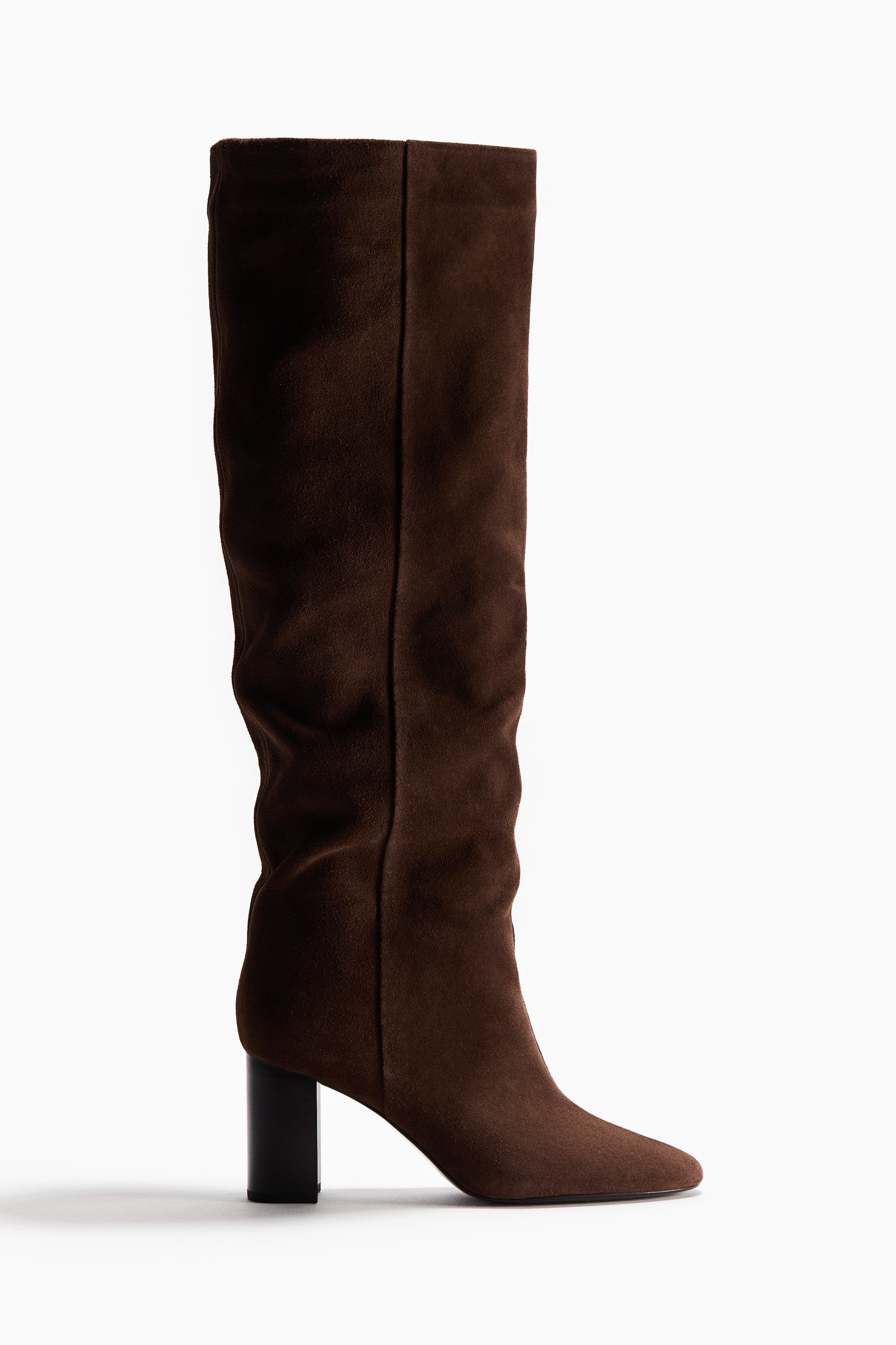 View larger image: A dark brown suede boot is standing, facing right. It is featuring an almond toe, a slouchy knee-high shaft, and a dark wood-look block heel.