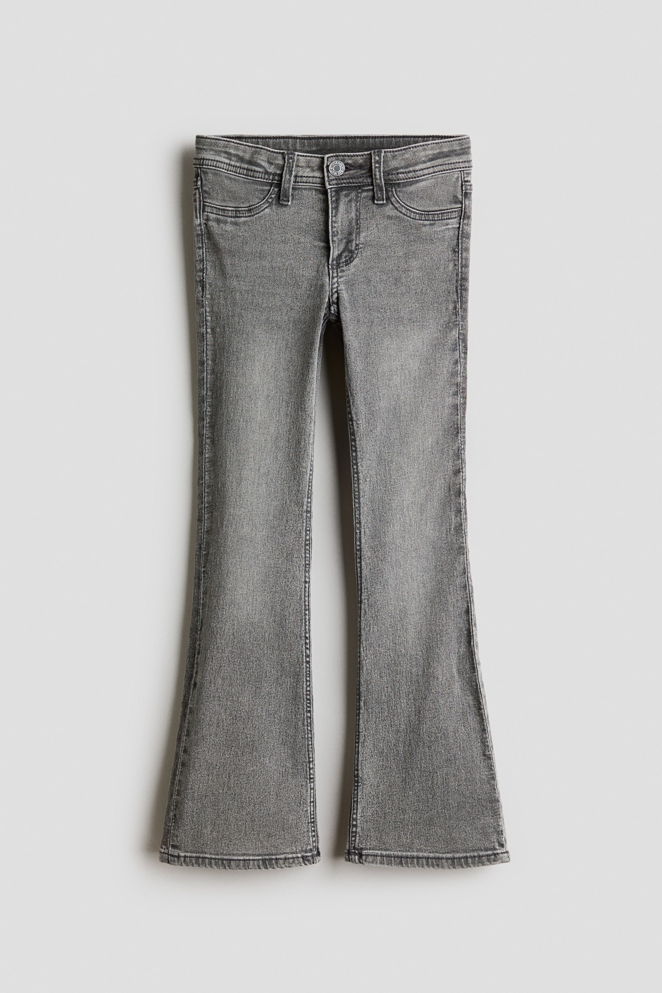 View larger image: Gray jeans are displayed front-facing, showcasing a low-waist, skinny fit through the hip and thigh with dramatically flared legs. The jeans feature a button and zip fly closure, with faux front pockets and visible belt loops.