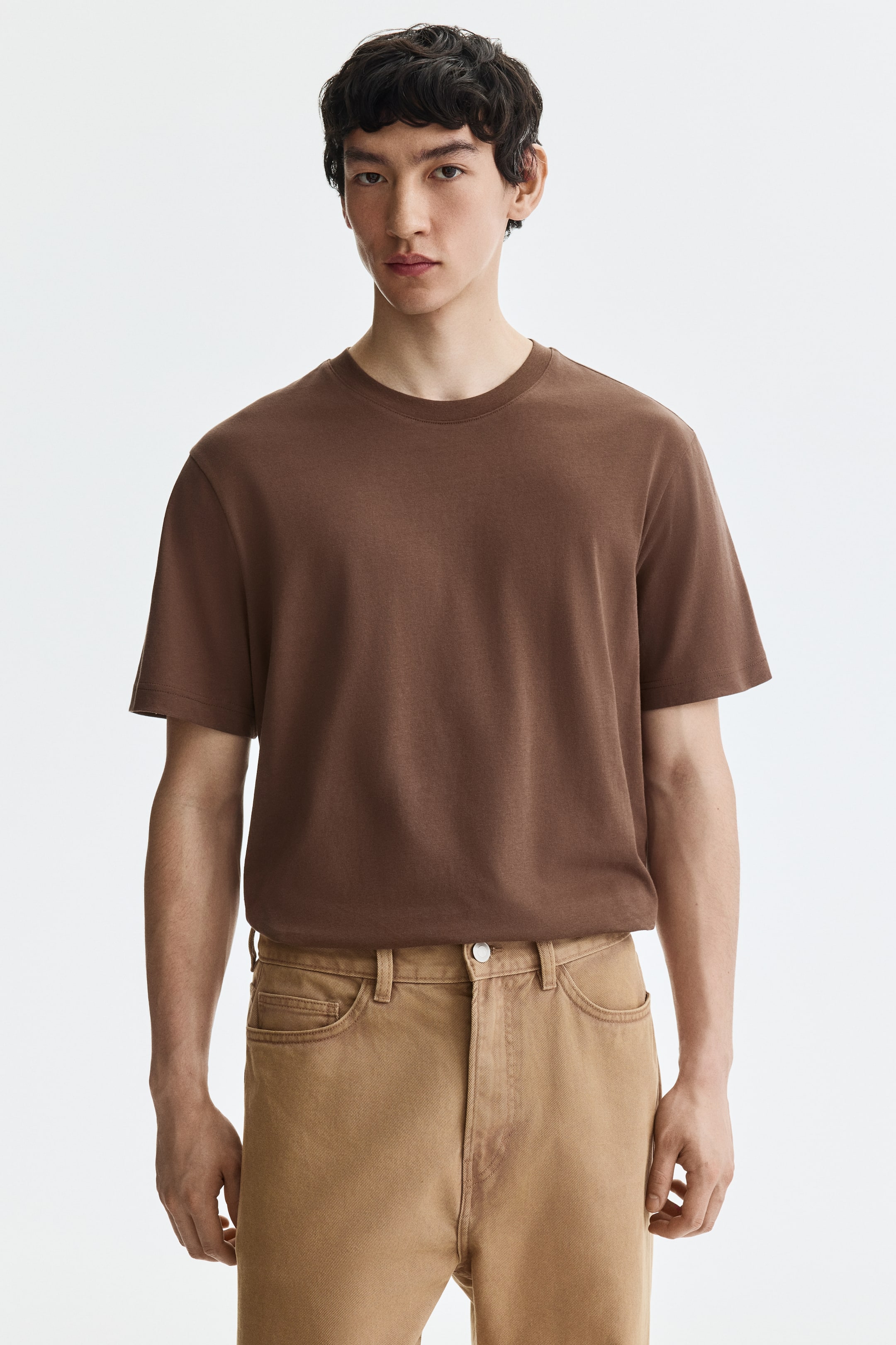Ver imagen más grande: Se muestra una camiseta marrón de cuello redondo desde el frente, con mangas cortas y un ajuste holgado, presentando una textura de tela suave.