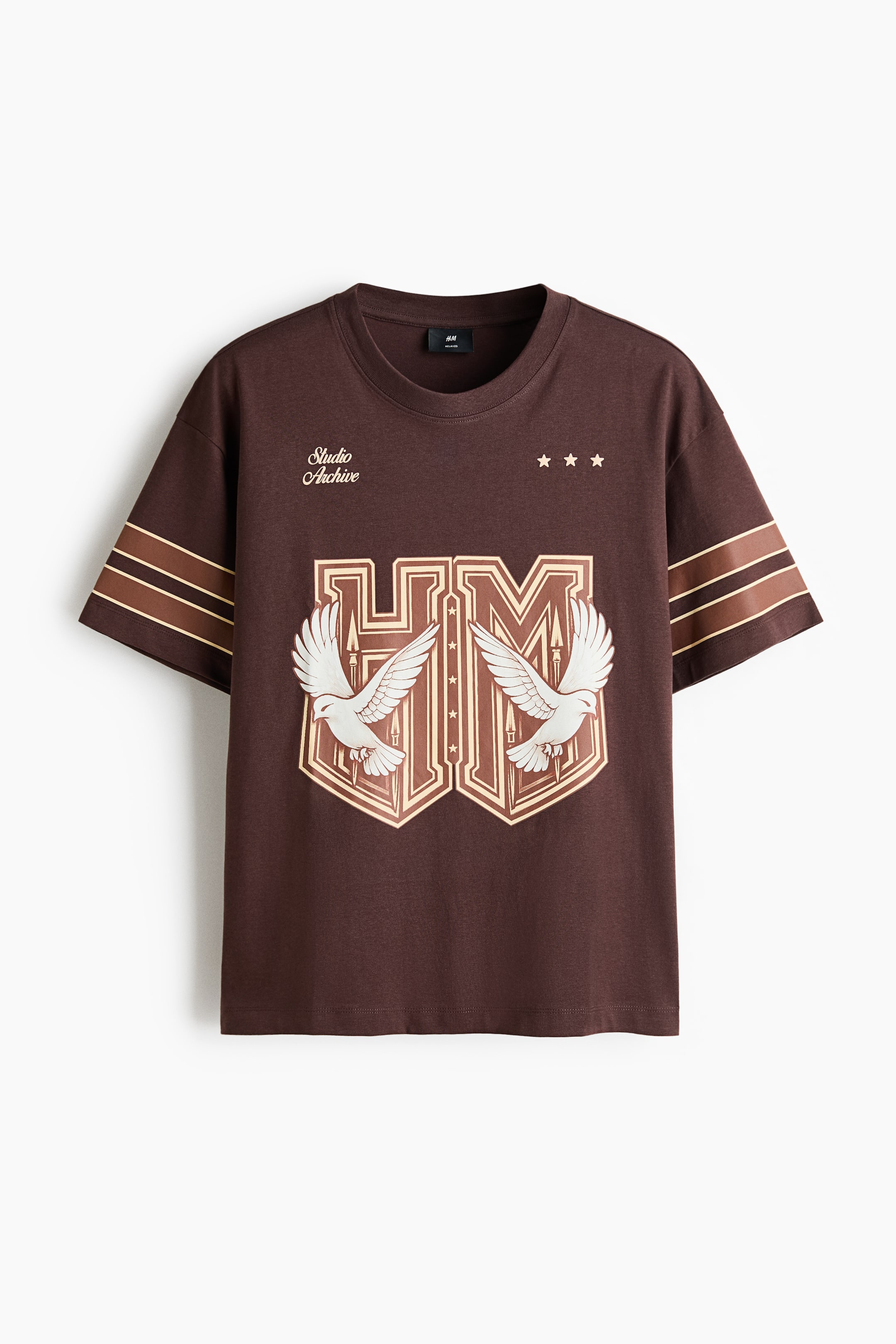 View larger image: A dark brown t-shirt is laid out flat, showcasing a round neck and short sleeves adorned with two contrasting horizontal stripes in light brown and dark brown. The front prominently displays a large central graphic featuring stylized "HM" letters within a shield, embellished with two white doves, accompanied by the text "Studio Archive" and three stars above.