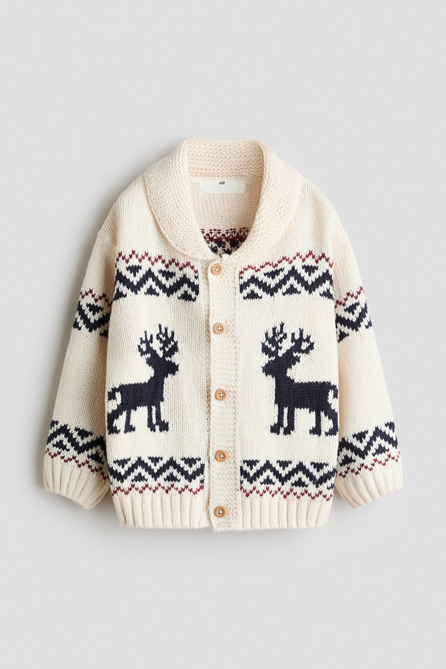 Eine Strickjacke in Offwhite ist von vorne zu sehen und verfÃ¼gt Ã¼ber einen dicken Schalkragen, einen Frontverschluss mit fÃ¼nf KnÃ¶pfen in Holzoptik sowie gerippte BÃ¼ndchen und Saum. Das Design zeigt auf der Brust zwei dunkelblaue Rentiersilhouetten, die einander zugewandt sind, eingefasst von geometrischen Fair-Isle-Mustern in Navy und Burgunderrot Ã¼ber den Rumpf und die Ãrmel.