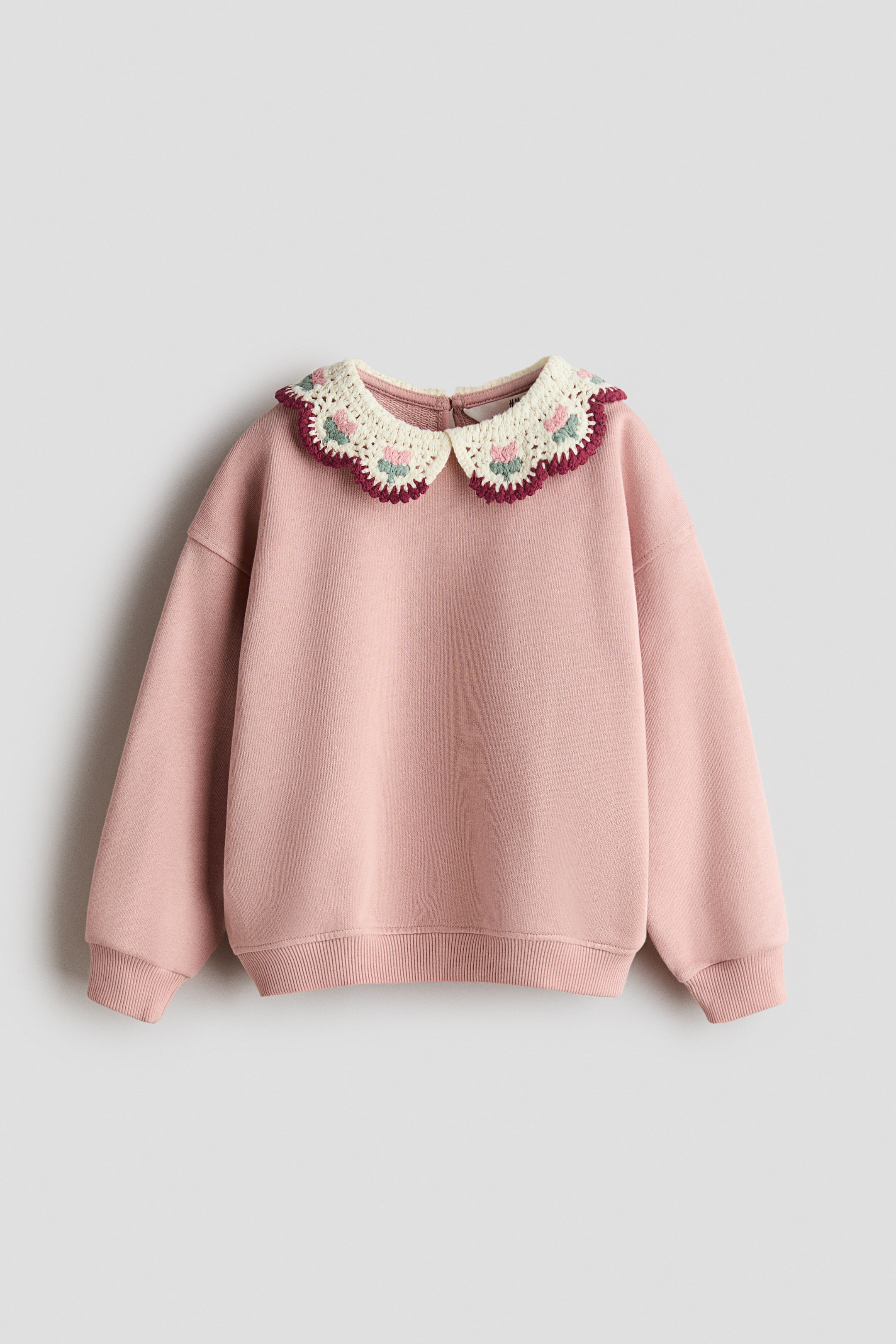 Visa större bild: En rosa sweatshirt visas framifrån och har en krämfärgad krage i virkad look med broderade blomdetaljer och en vågad kant i burgundy. Plagget har nedhasade axlar, långa ärmar med ribbade muddar och en ribbad nederkant.