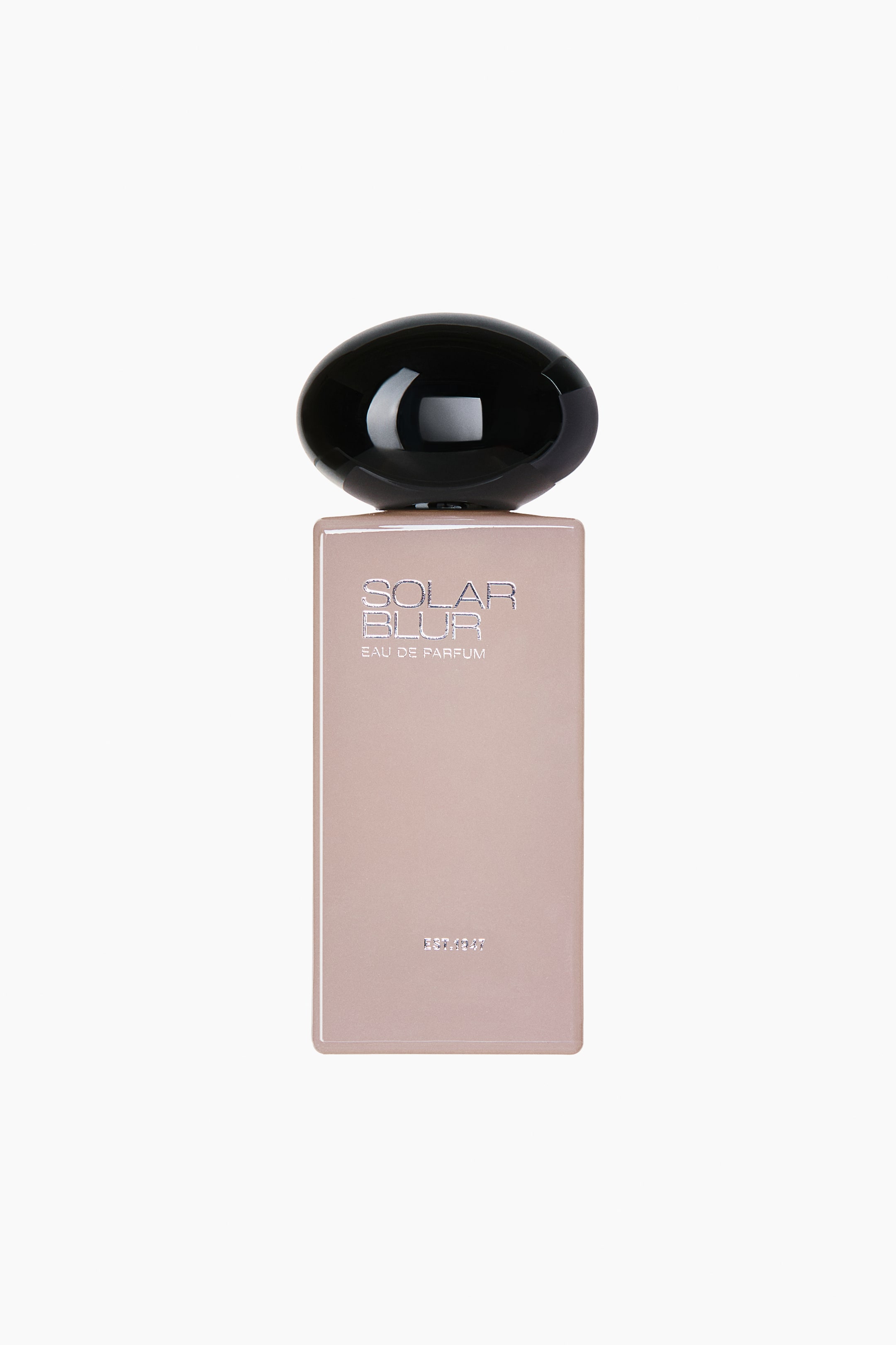 Größeres Bild anzeigen: Die Solar Blur EdP-Flasche steht aufrecht und zeigt die Vorderansicht ihres hohen, rechteckigen, glänzenden Körpers in Nude-Rosa sowie ihre große, abgerundete, glänzend schwarze Kappe. Oben ist der silberfarbig gravierte Text „SOLAR BLUR“ und „EAU DE PARFUM“ zu sehen, während nahe dem unteren Bereich „EST. 1947“ erscheint.