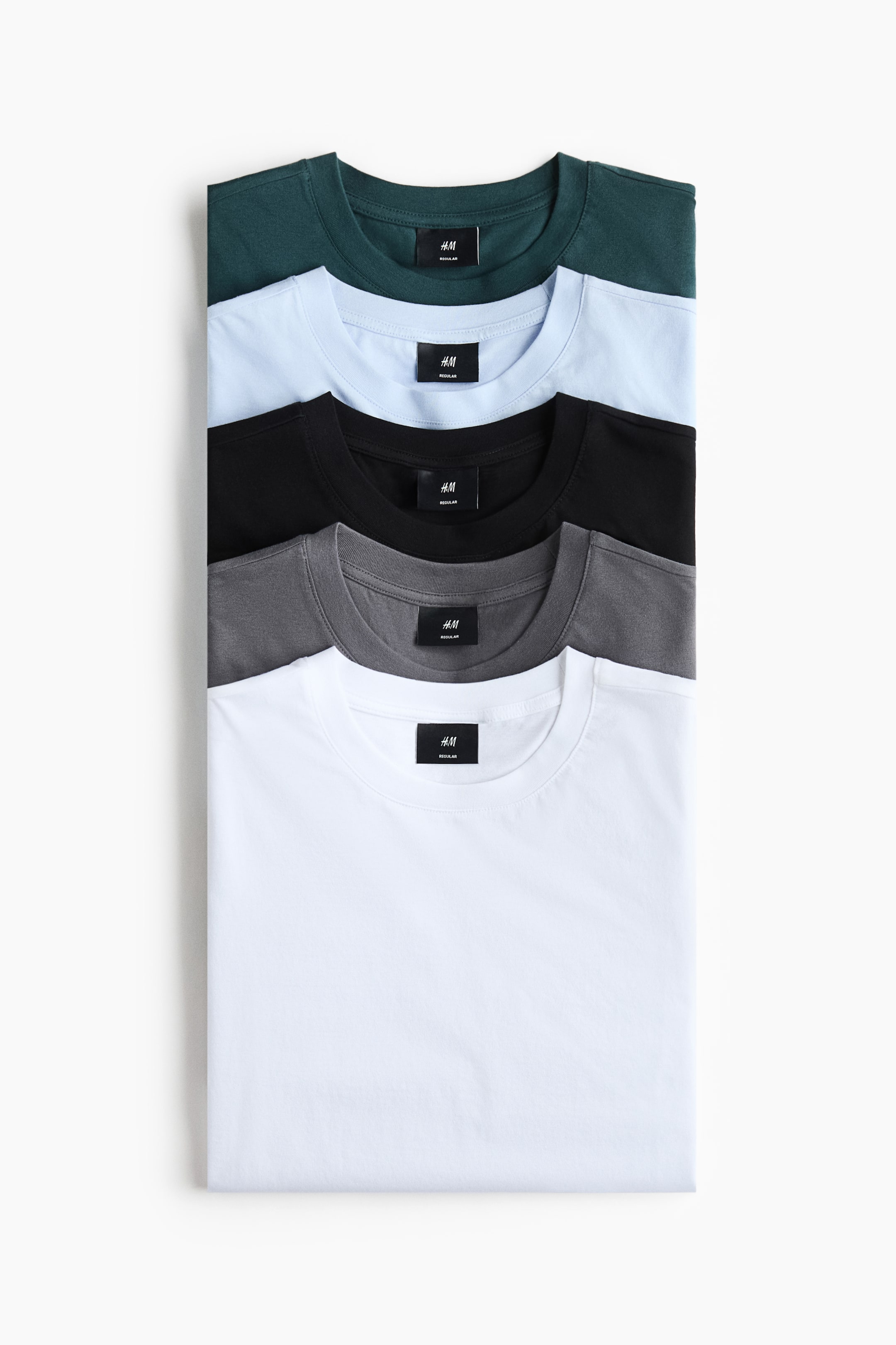 View larger image: Five T-shirts are stacked front-facing, showcasing round, ribbed necklines with black brand labels and straight-cut hems. The T-shirts are available in dark green, light blue, black, dark gray, and white.