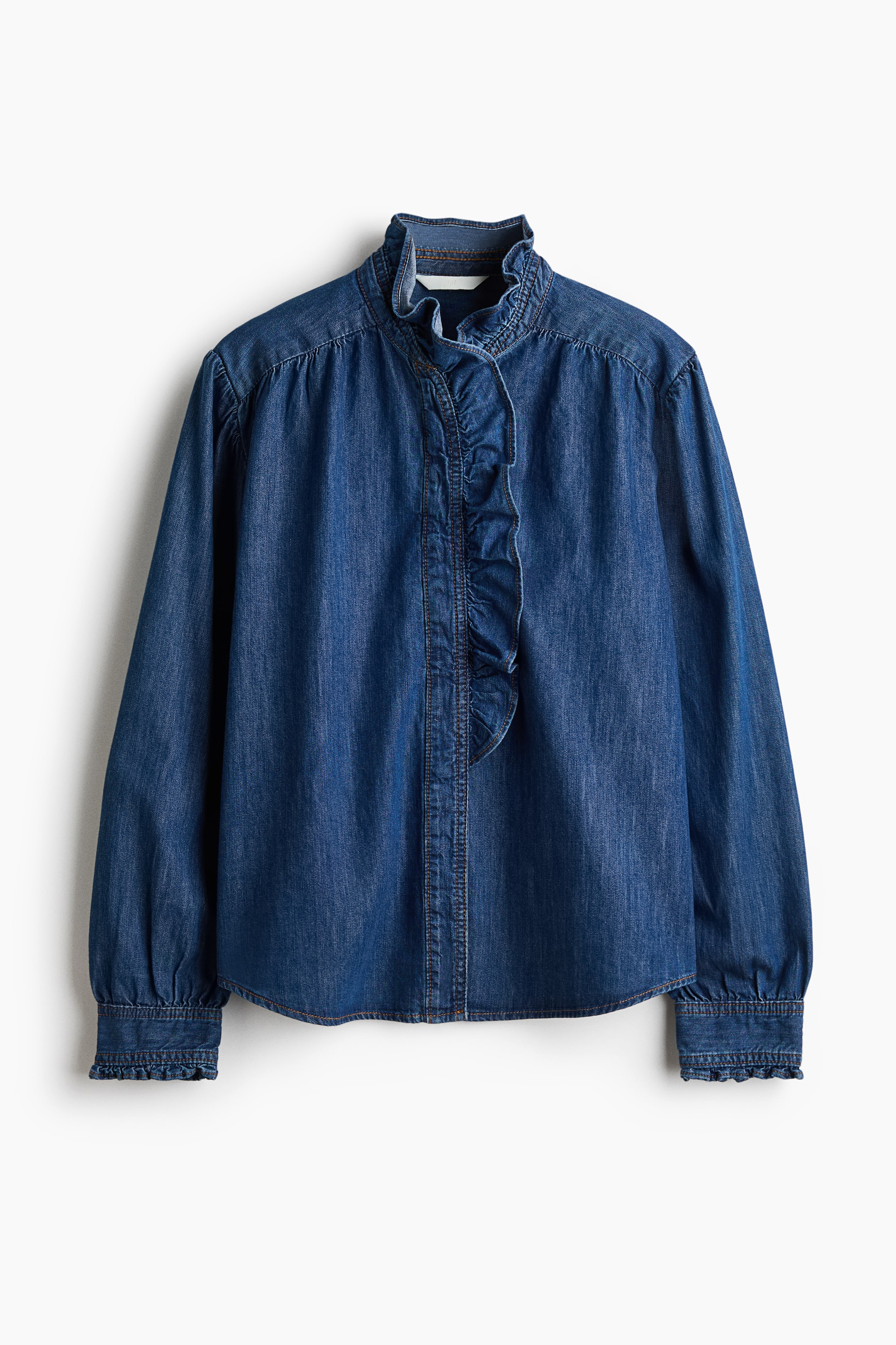 View larger image: A blue denim blouse featuring a ruffled stand-up collar, a ruffled placket running down the centre front, and long sleeves with gathered shoulders and ruffled cuffs.