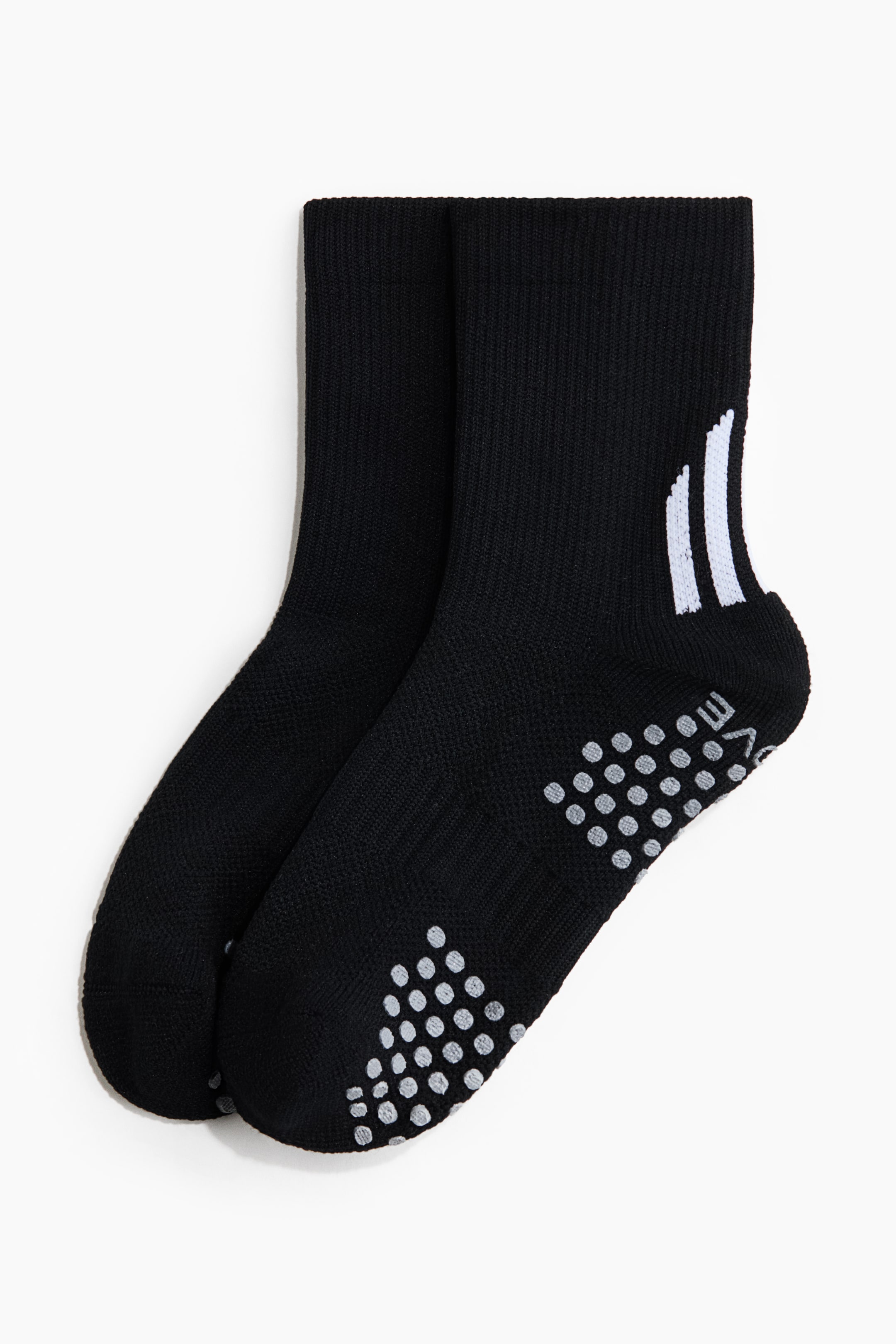 View larger image: Black football socks feature a soft fine knit, with high ribbed legs and elasticated tops. They showcase grip soles covered in numerous light gray dots, and one sock displays three white stripes on its outer side.