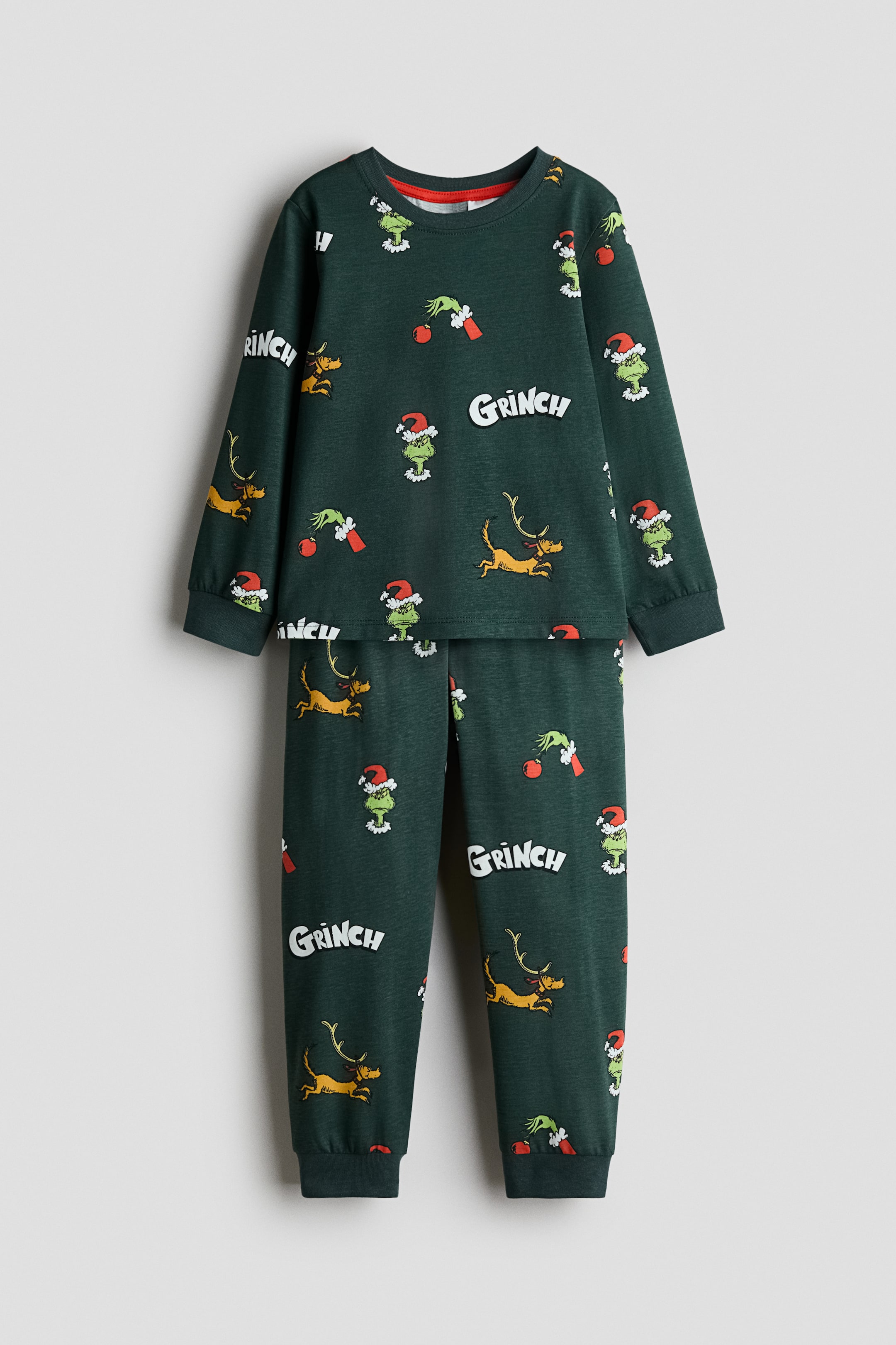View larger image: A dark green pajama set is shown from the front, featuring a long-sleeved top and matching pants with an all-over print of Grinch-themed characters and text. The top is designed with a round, ribbed neckline and ribbed cuffs, while the pants feature an elasticated waistband and ribbed hems.