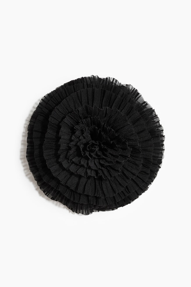 A black fabric rosette accessory is facing front, showcasing concentric layers of finely pleated, sheer black ruffles that spiral toward a clustered center. The ruffles are creating a textured, dimensional flower shape with delicate, crimped edges. - 1