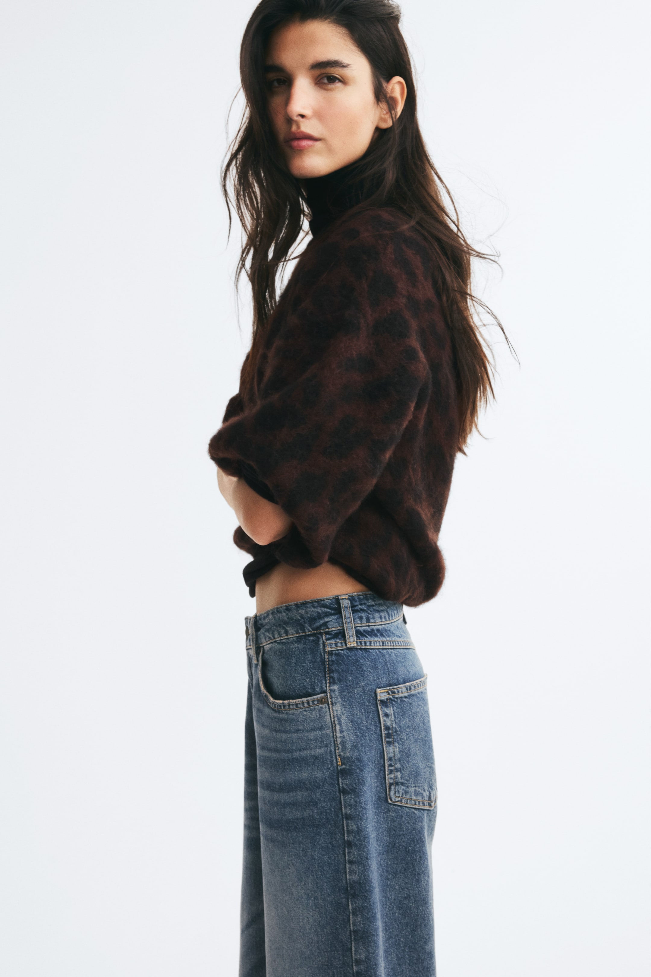 View larger image: A brushed jacquard knit sweater with a dark brown and black animal print is worn by the model, who is standing in profile with arms crossed. The sweater features dropped shoulders and three-quarter-length sleeves, and is layered over a black turtleneck and paired with blue jeans.