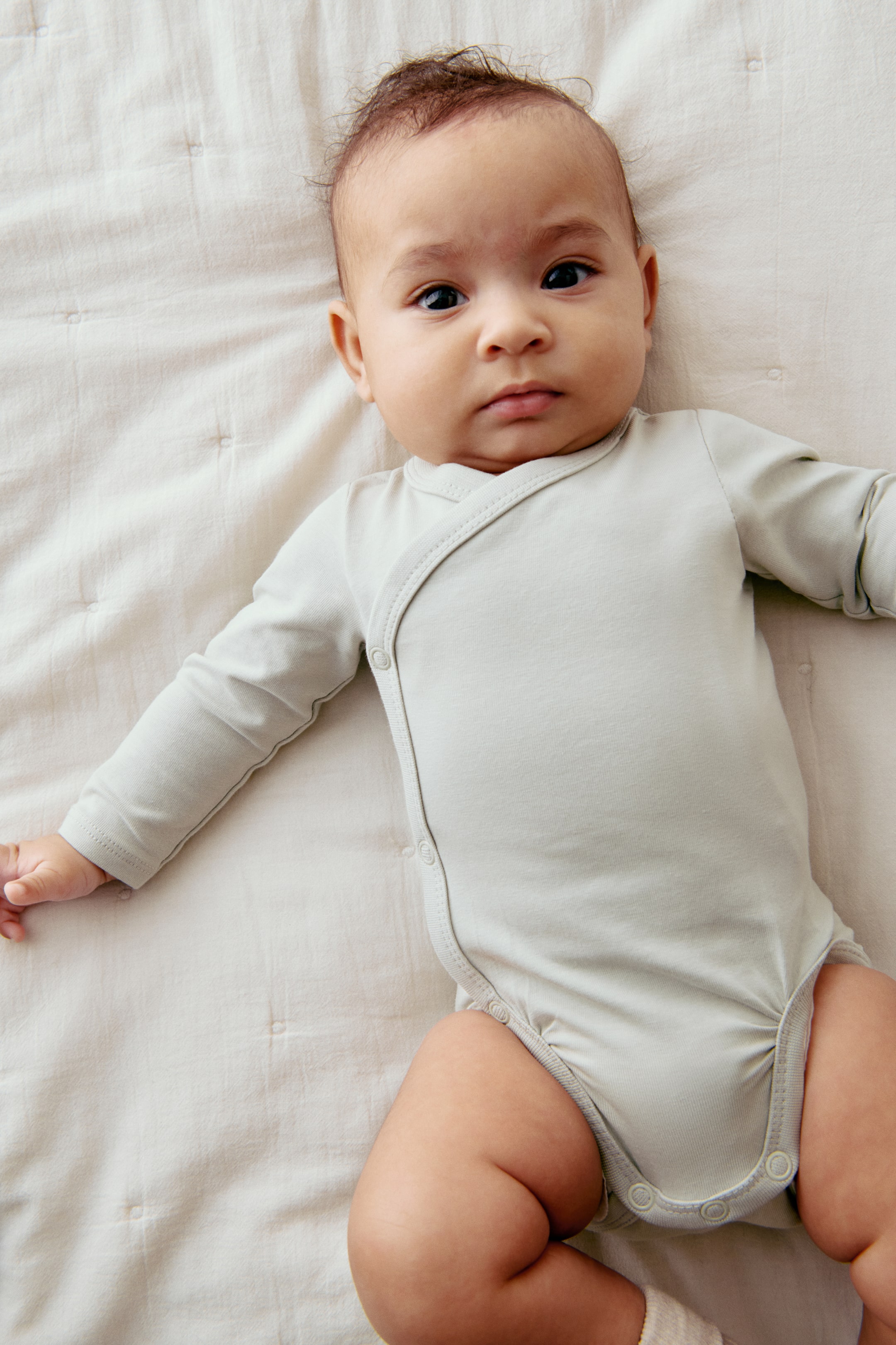 查看大圖: 穿著一件淺灰色針織長袖裹身連體衣，特色是左側和襠部有按扣設計。