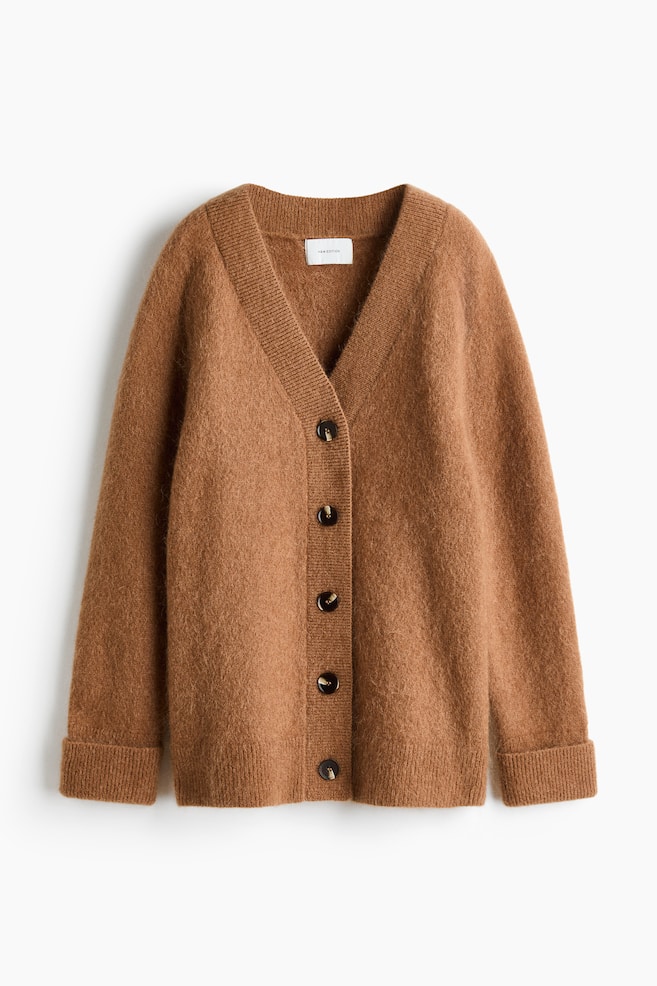 An oversized brown knit cardigan is shown from the front, featuring a deep ribbed V-neckline and a five-button front fastening. The soft, fuzzy garment has long raglan sleeves with wide ribbed cuffs and a matching ribbed hem. - 1