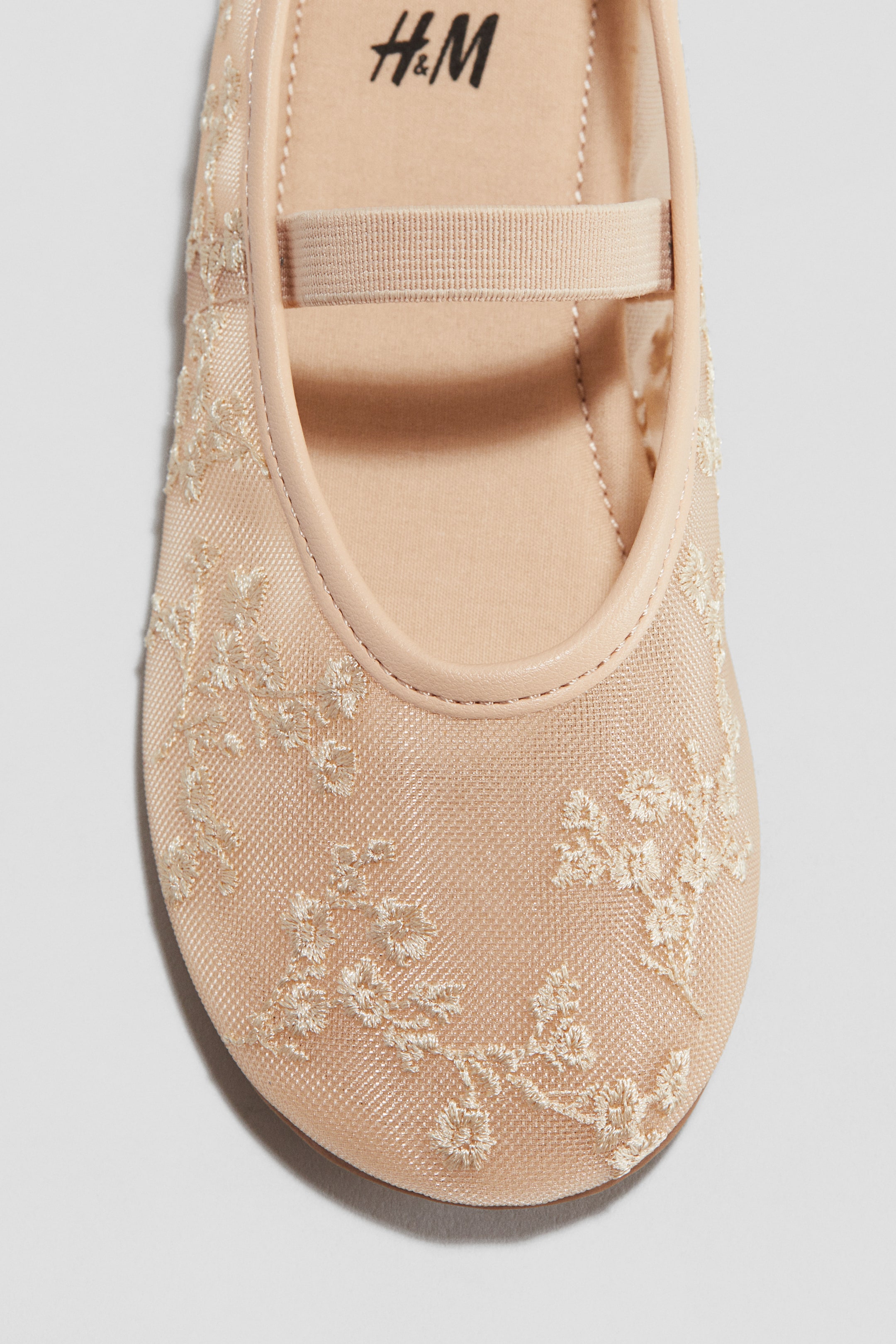 View larger image: A light beige Mary Jane shoe is featuring a rounded toe box in sheer mesh, adorned with delicate light-colored floral embroidery. An elastic strap is stretching across the instep, and a smooth binding is trimming the shoe's opening, with the 'H&M' logo visible on the insole.
