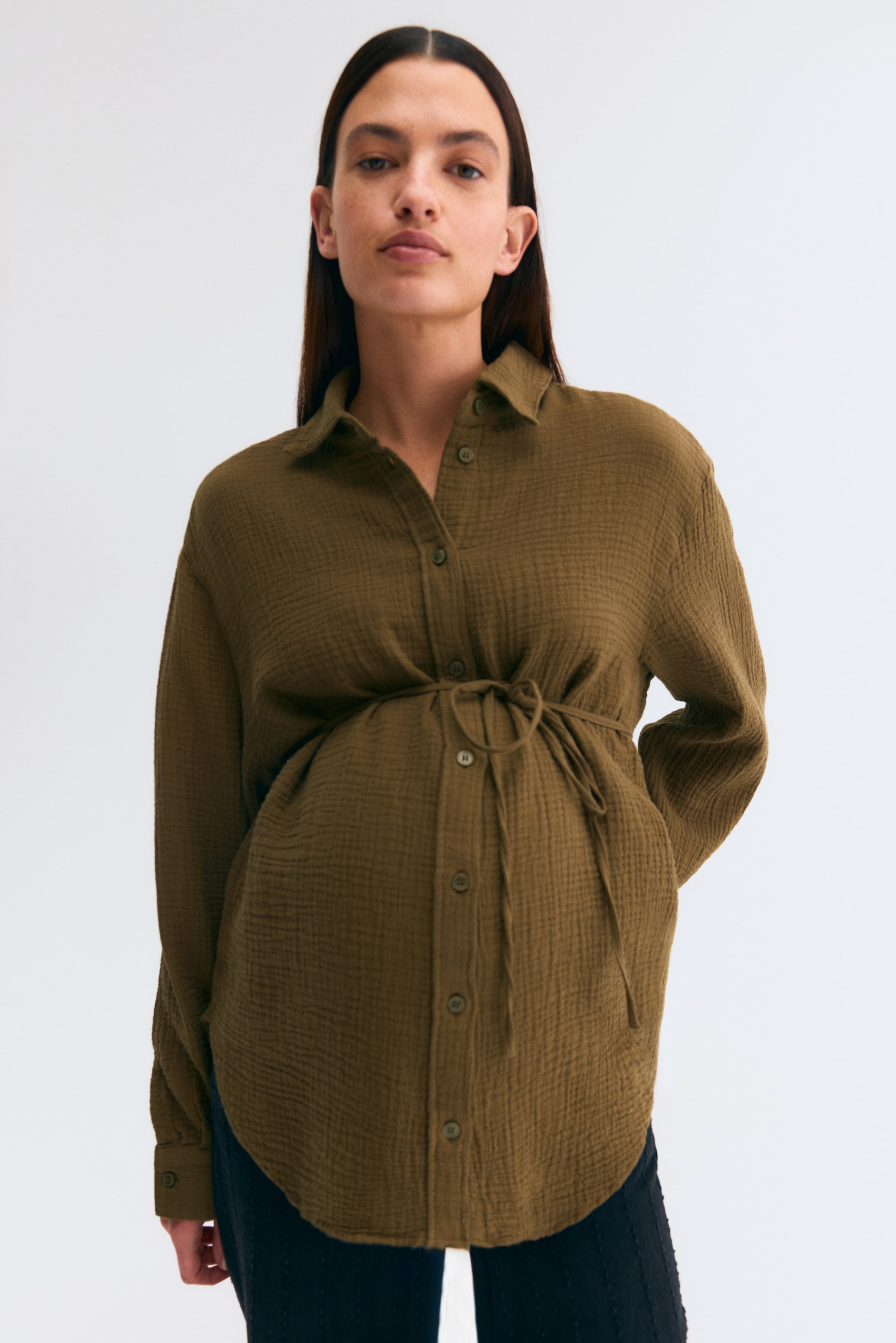 View larger image: The olive-green crinkled shirt features a pointed collar, a button-front closure, and long sleeves, and is cut with a rounded hem. A drawstring at the waist is tied to cinch the shirt, creating a gathered, relaxed fit.