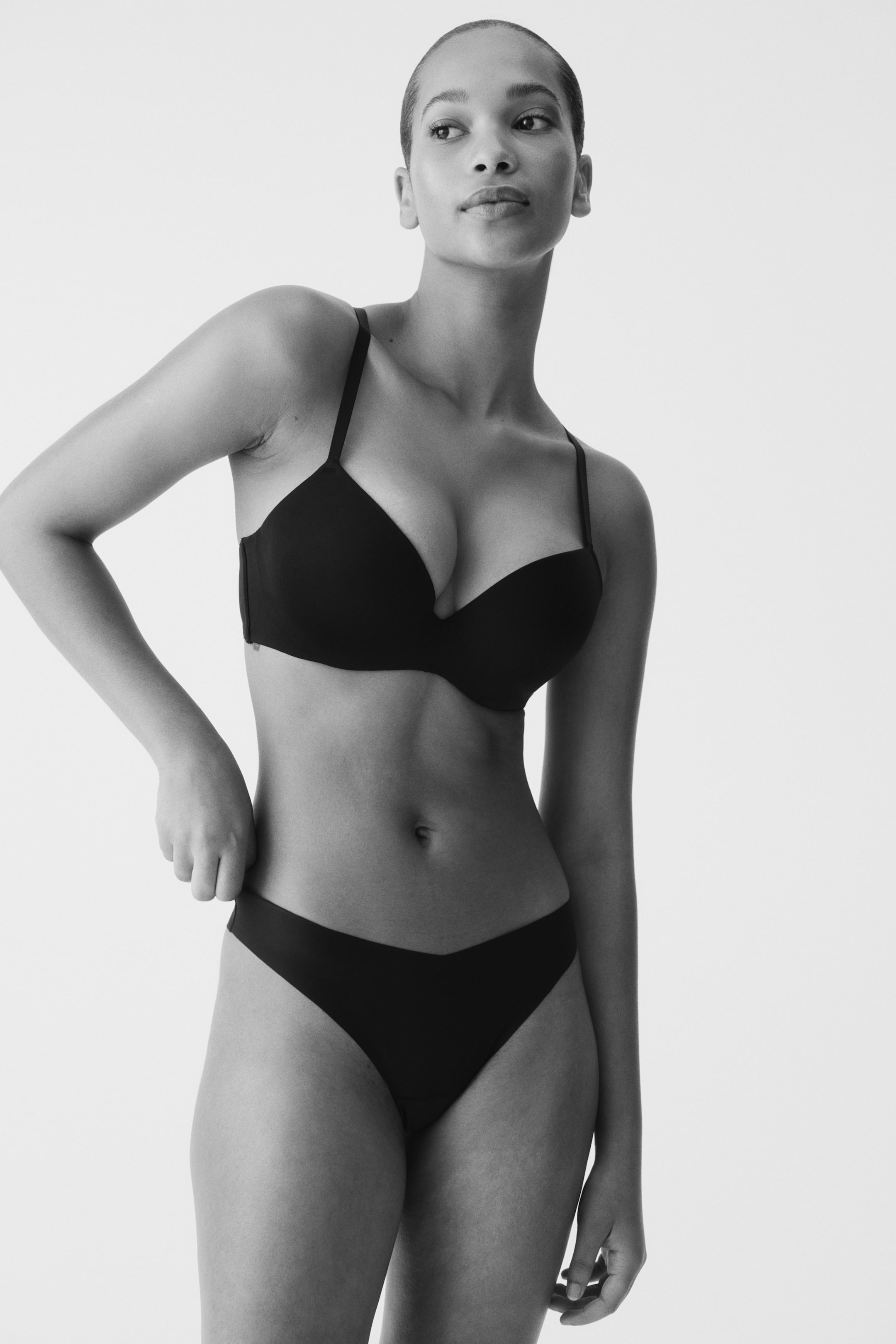 Grösseres Bild ansehen: Ein schwarzer Push-up-BH mit glatten, geformten Cups und dünnen Trägern. Passende Low-Rise-Bikini-Unterwäsche mit einem V-förmigen Bund vorne, beide Artikel aus der Frontansicht präsentiert.