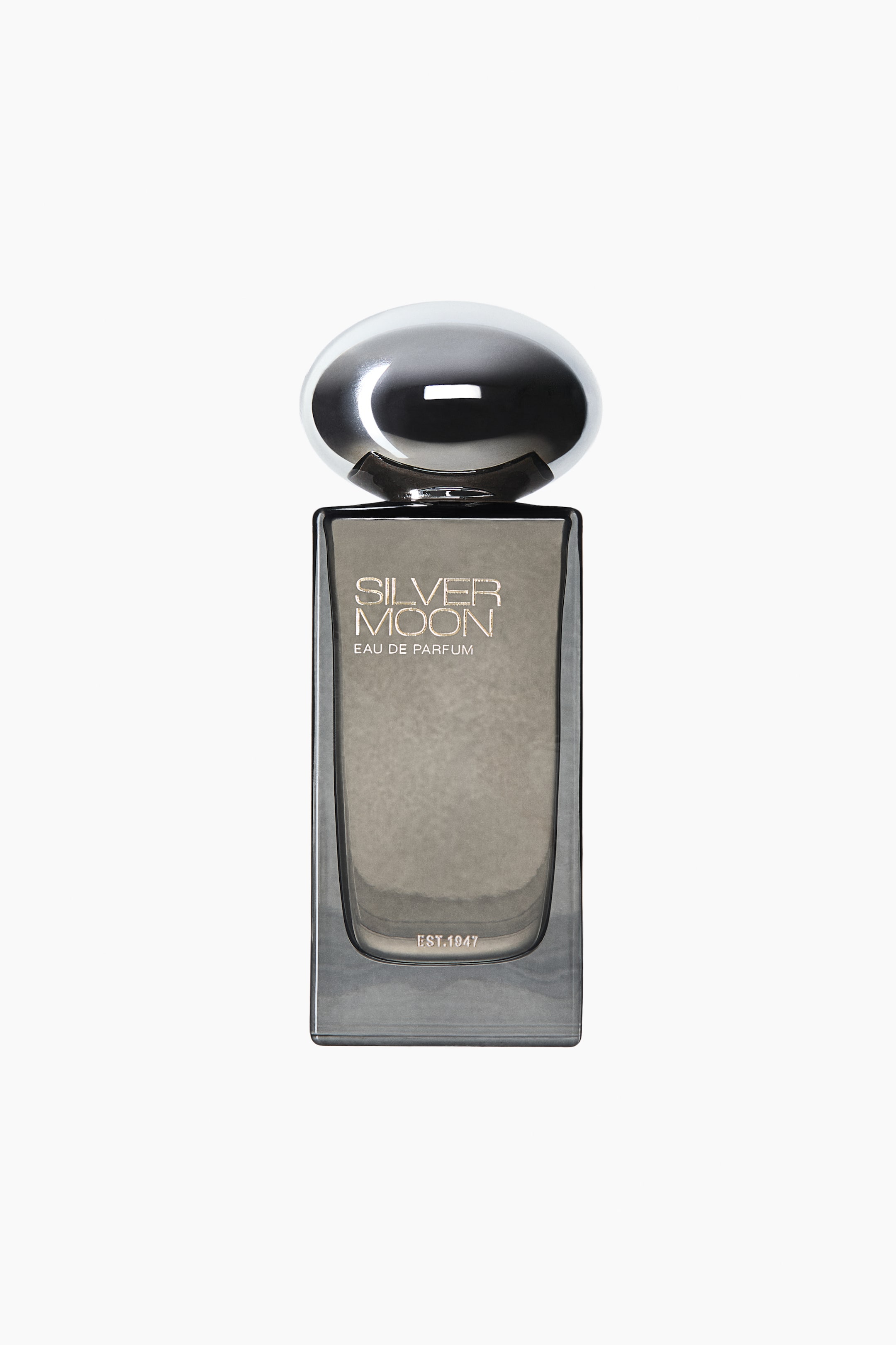 Vis større bilde: En frontvisning av Silver Moon Eau de Parfum-flasken vises, med en rektangulær glasskropp med gråtonet finish og et avrundet indre reservoar. Flasken fremhever en stor, polert sølvfarget kuppelformet kork og viser teksten «SILVER MOON» og «EAU DE PARFUM» i sølvfarget skrift på forsiden.