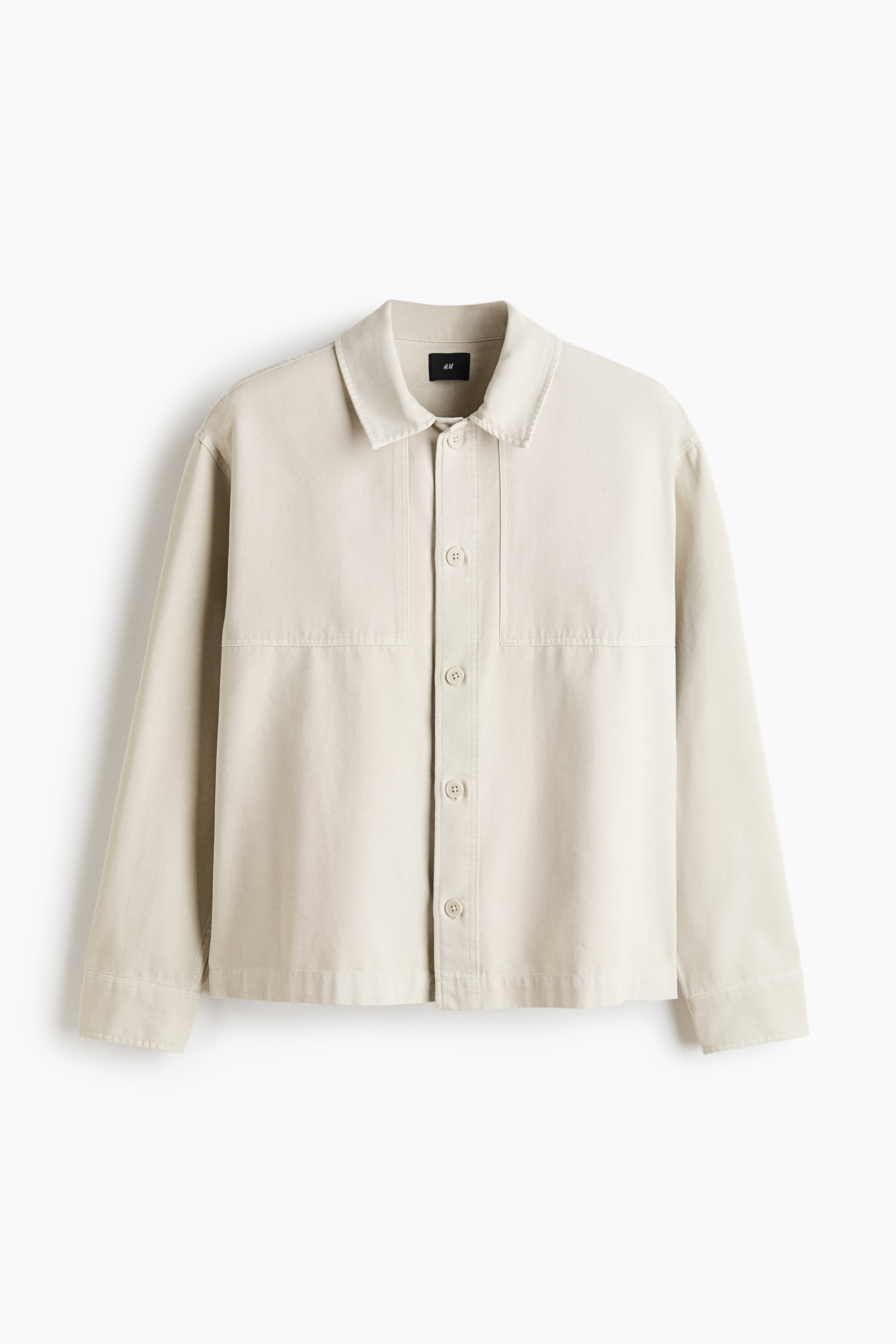 View larger image: A light beige jacket is showcased in a front view, featuring a pointed collar, a full button-front closure with tone-on-tone buttons, long sleeves with straight cuffs, and horizontal and vertical seam detailing on the front panels.