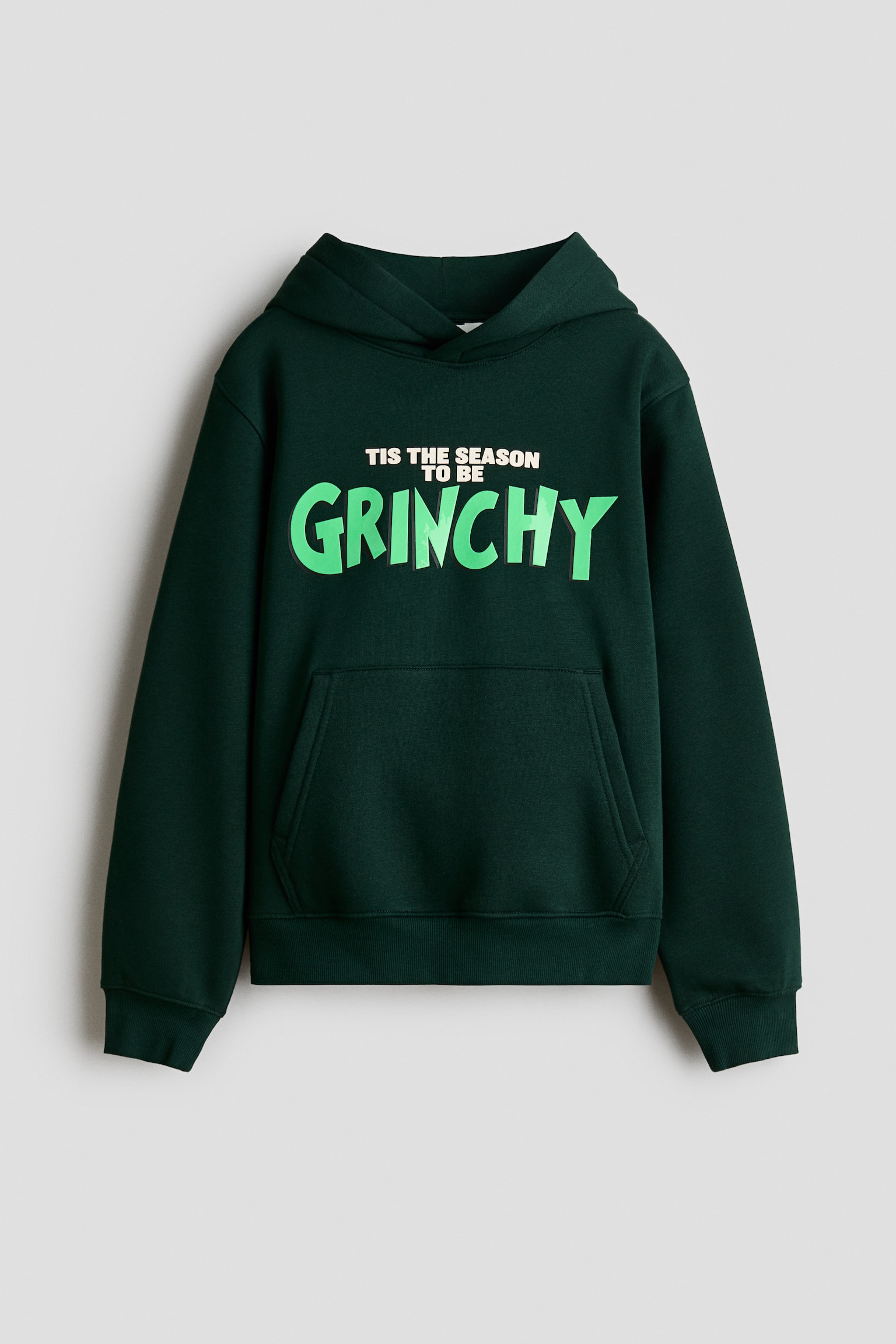 Un chandail Ã  capuchon vert foncÃ© est prÃ©sentÃ© de face, avec un capuchon croisÃ©, des Ã©paules tombantes, des manches longues et une poche kangourou Ã  lâavant. La poitrine affiche un motif imprimÃ© portant lâinscription Â« TIS THE SEASON TO BE GRINCHY Â» en blanc et vert vif, tandis que des poignets cÃ´telÃ©s et un ourlet cÃ´telÃ© complÃ¨tent le design.