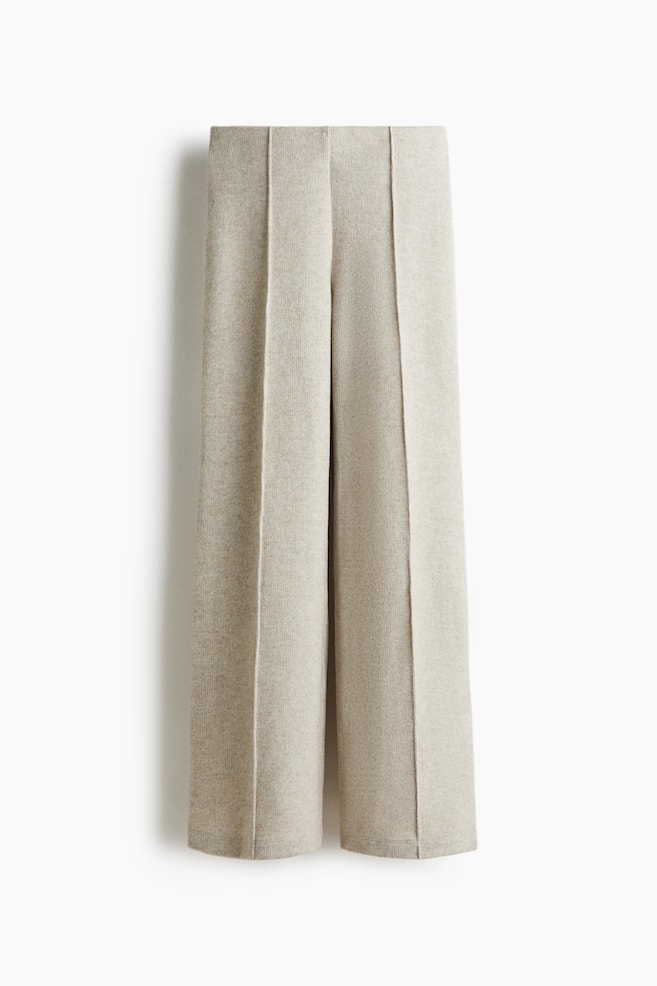 Un paio di pantaloni in maglia mélange beige chiaro è esposto in piano, presentando una vista frontale con gambe larghe e pieghe nette e permanenti che corrono lungo il centro di ciascuna gamba. - 1