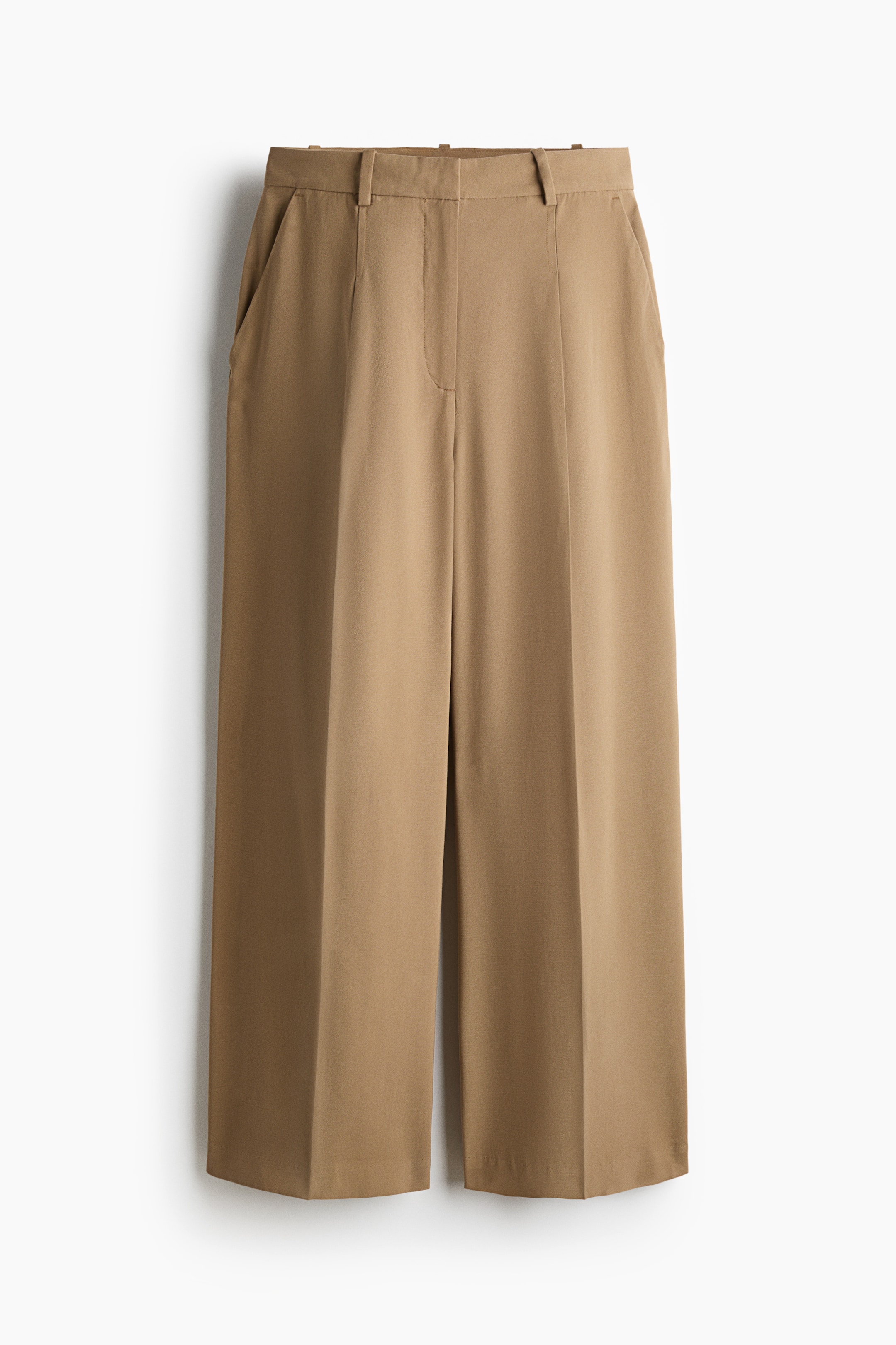View larger image: These beige wide-leg trousers are hanging front-facing, featuring a structured waistband with belt loops and side slash pockets. The trousers showcase a relaxed silhouette with sharp, vertical pressed creases running down the centre of each leg.