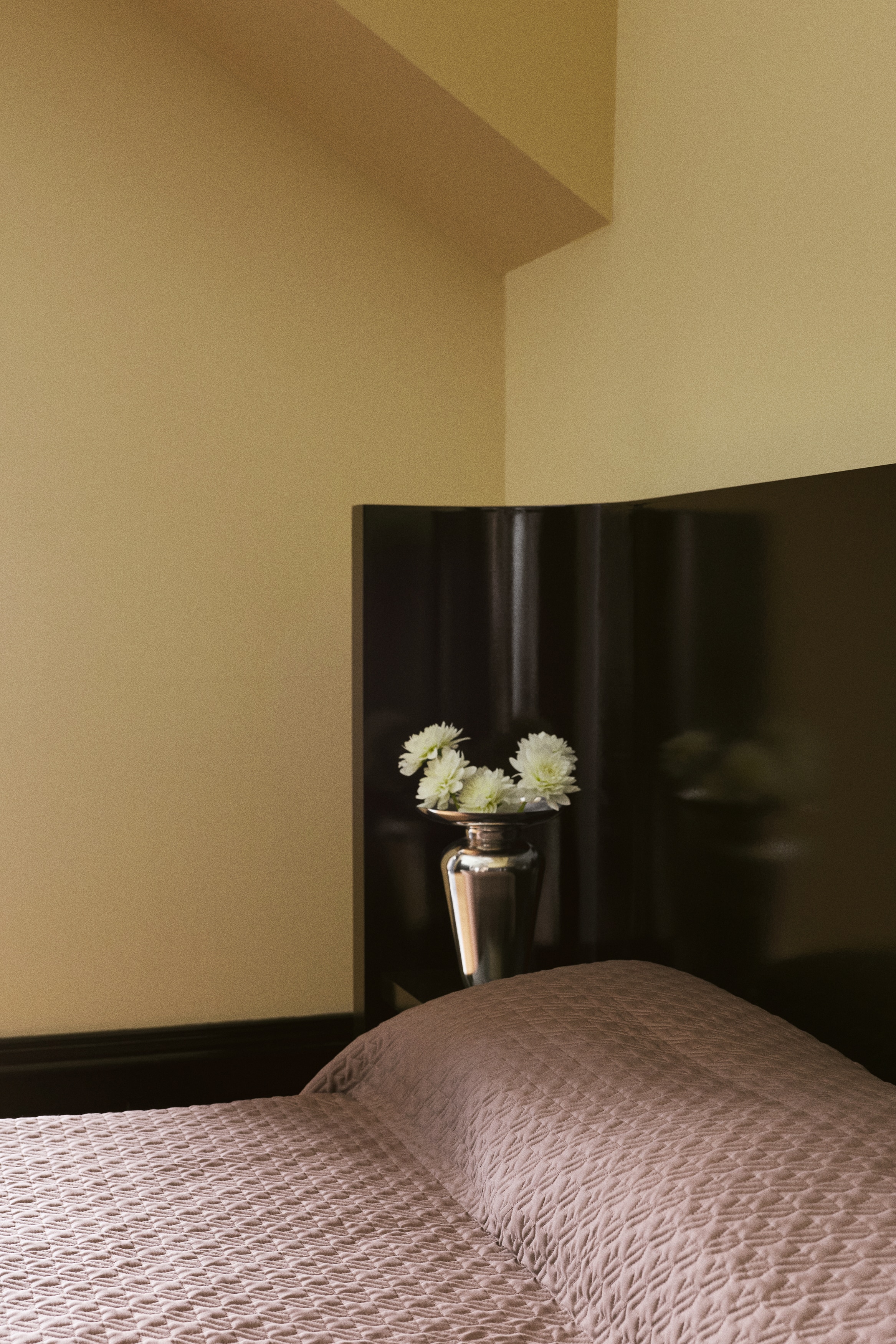 A brown quilted blanket showcases a repeating stepped geometric stitch pattern across its surface. It features a plain, smooth border along its edges.