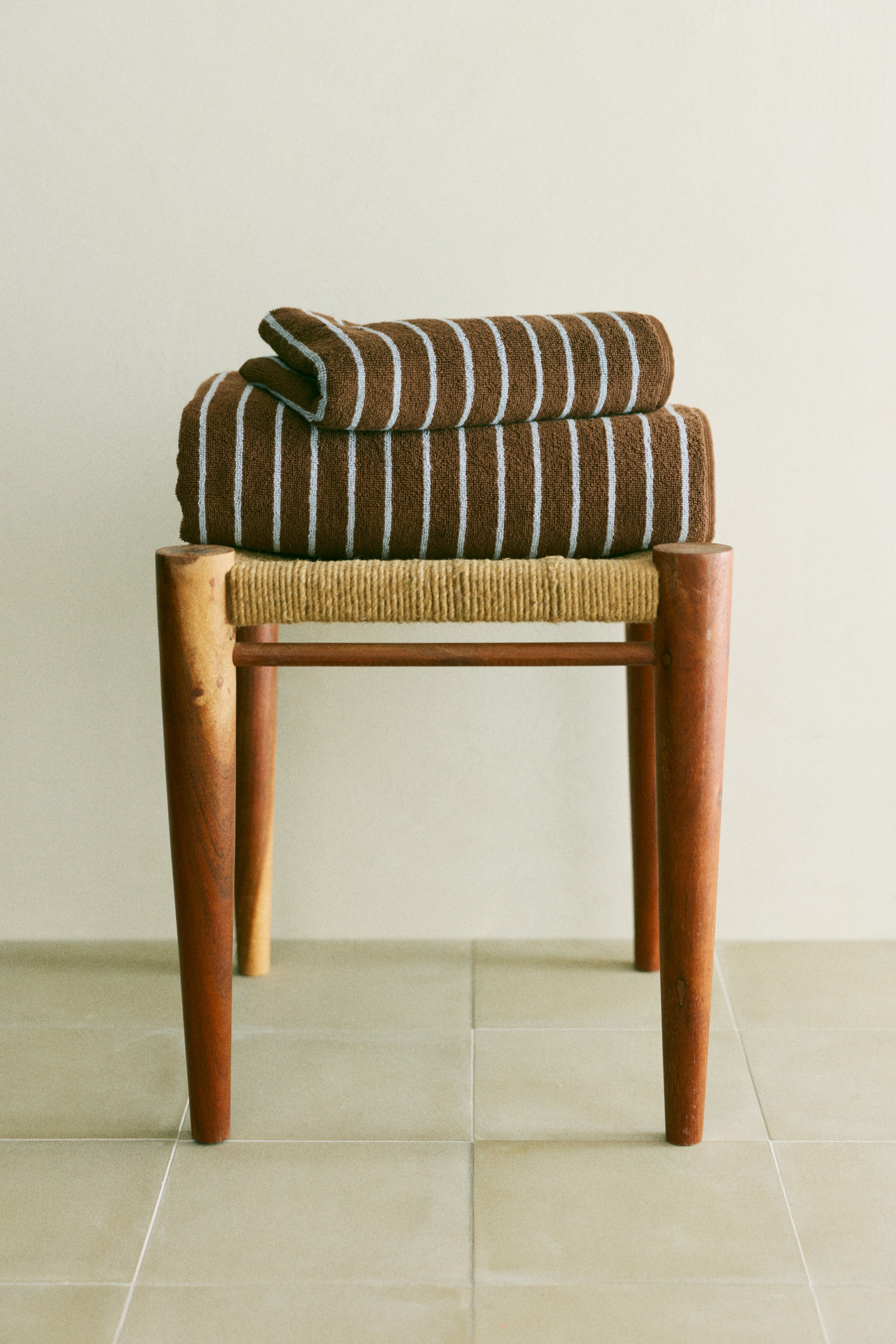 View larger image: Two brown towels, featuring light blue vertical stripes, are neatly folded and stacked, with one towel placed atop the other, on a stool.