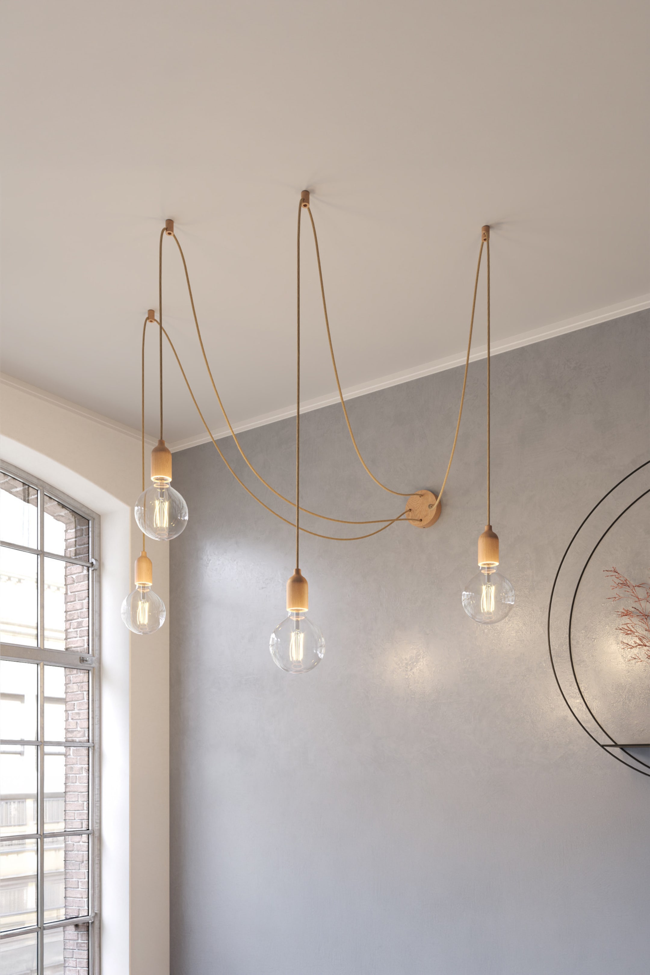 Größeres Bild ansehen: Ein mehrflammiges Pendelleuchten-Design präsentiert fünf klare, kugelförmige Glühbirnen, jede mit einer hellen Holzfassung. Hellbraune, stoffüberzogene Kabel hängen die Glühbirnen von der Decke und verbinden sie mit einer zentralen, kreisförmigen Holzhalterung an der Wand, die in einem künstlerischen Muster sichtbar drapiert ist. Die Glühbirnen strahlen ein warmes Licht aus.