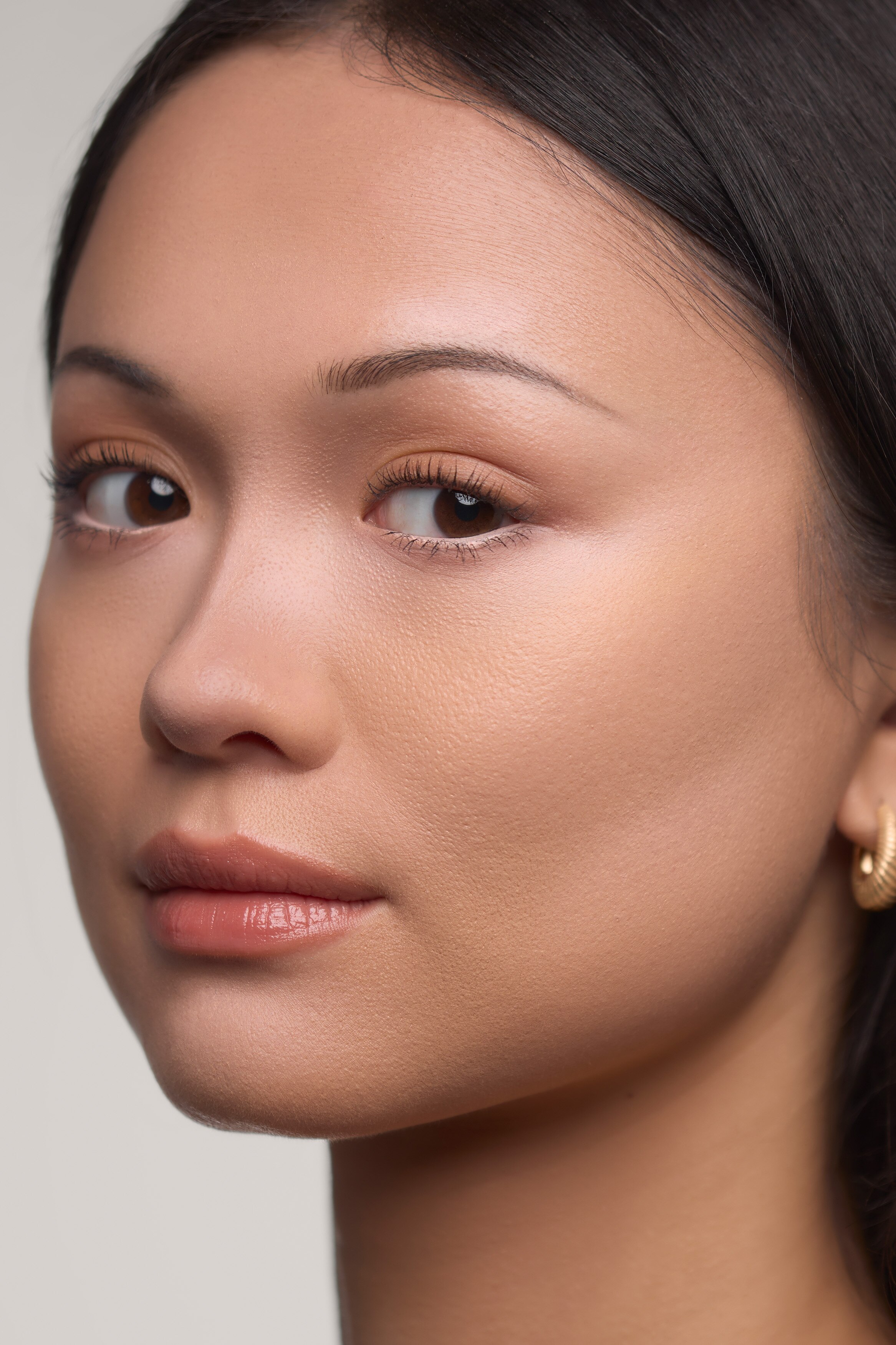 Morphe Shapelifter Micro Brightening Stick står loddrett og viser et slankt, hvitt etui med merkenavnet trykt vertikalt i grått. En avrundet, lys rosa produkttupp stikker ut fra den avsmalnede toppkragen, og matcher den lys rosa bunnhetten nederst.