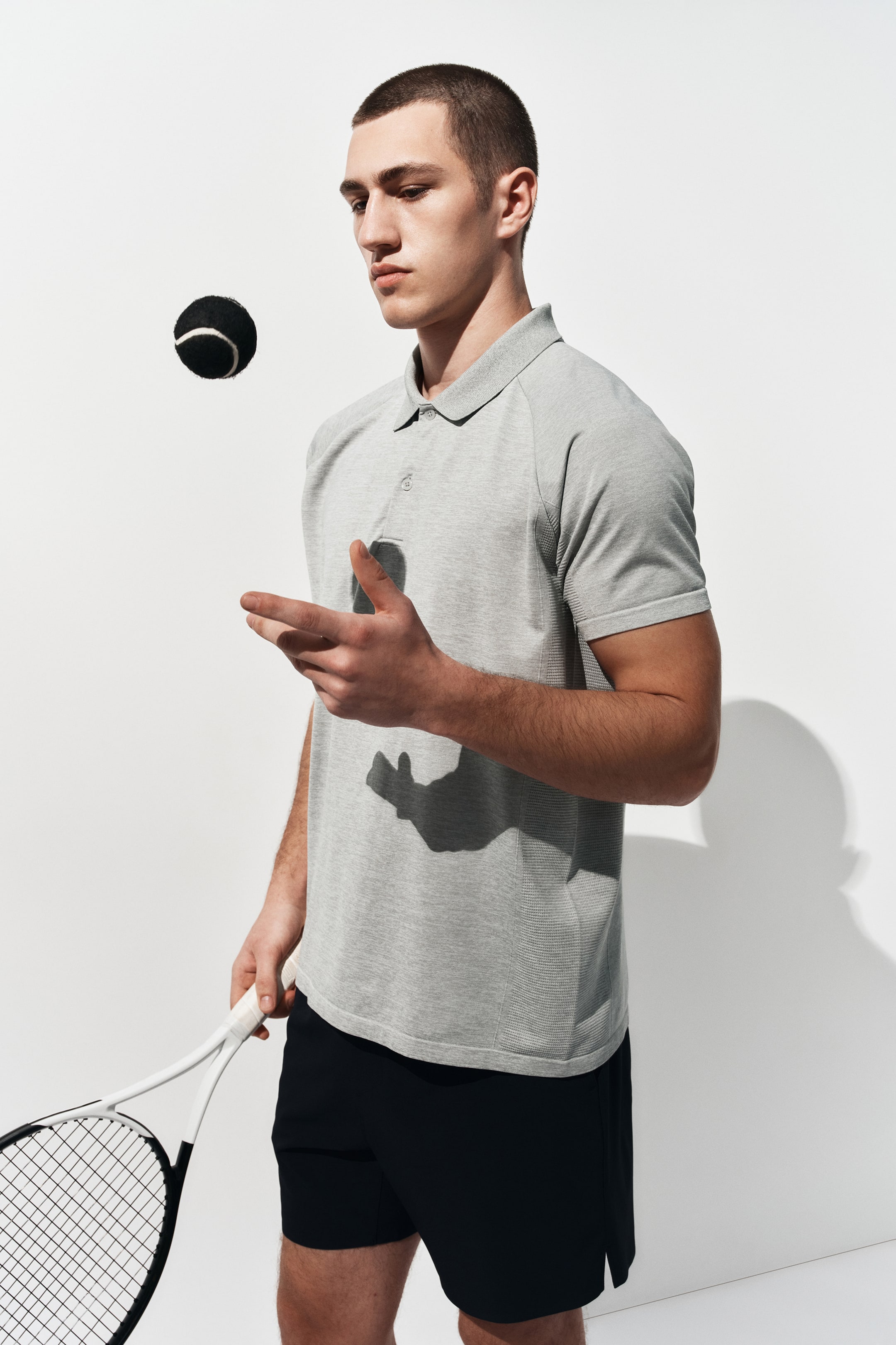 View larger image: A grey polo shirt featuring a pointed collar, a two-button placket, and raglan short sleeves with ribbed texture, showcasing a subtly textured body from a slightly angled front-side view.