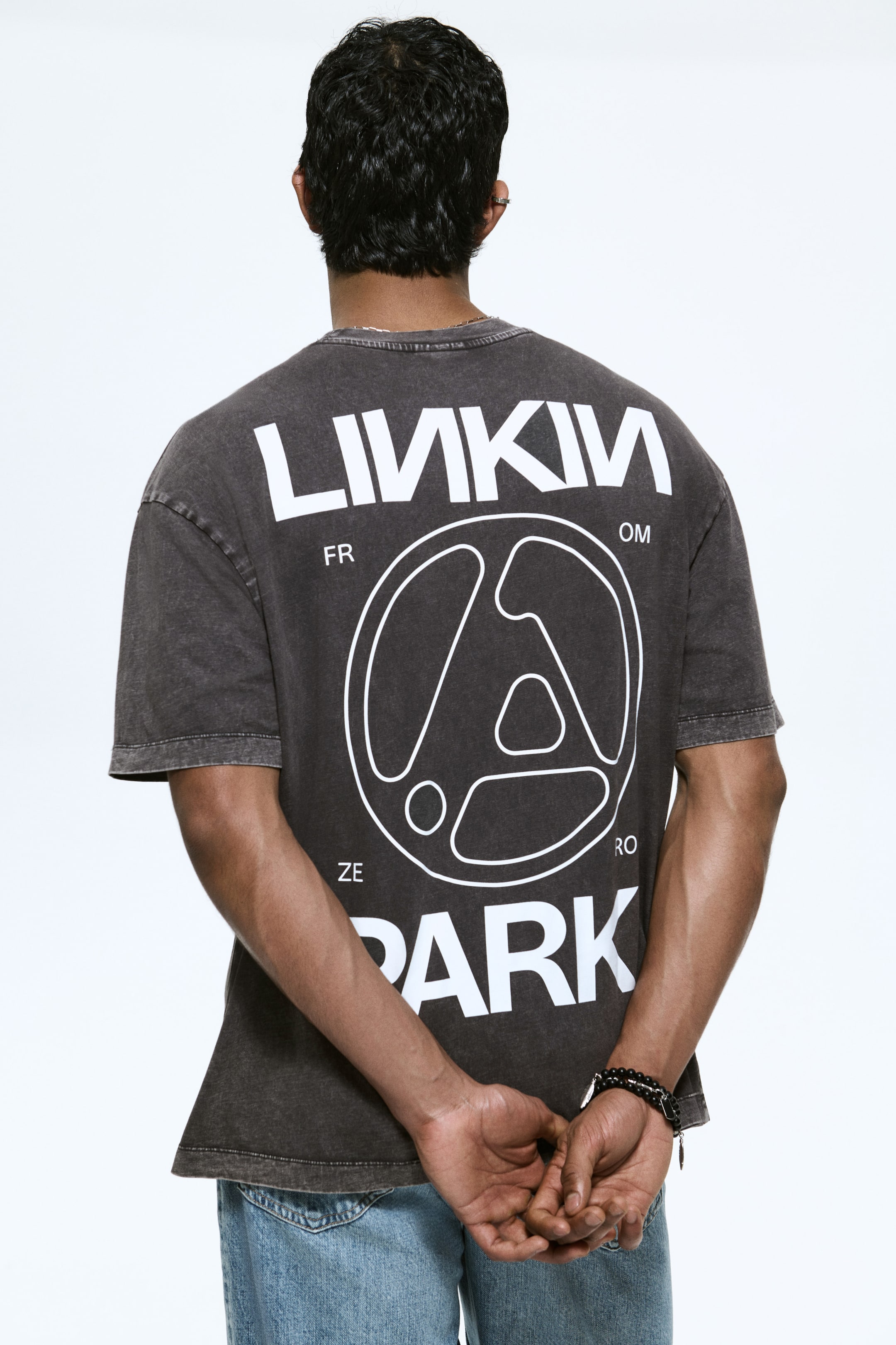 View larger image: A dark grey, washed T-shirt is shown from the back, featuring an oversized fit and short sleeves. A large white graphic dominates the back, with “LINKIN” across the top, “PARK” across the bottom, and a circular abstract logo with “FR OM ZE RO” text around its perimeter.