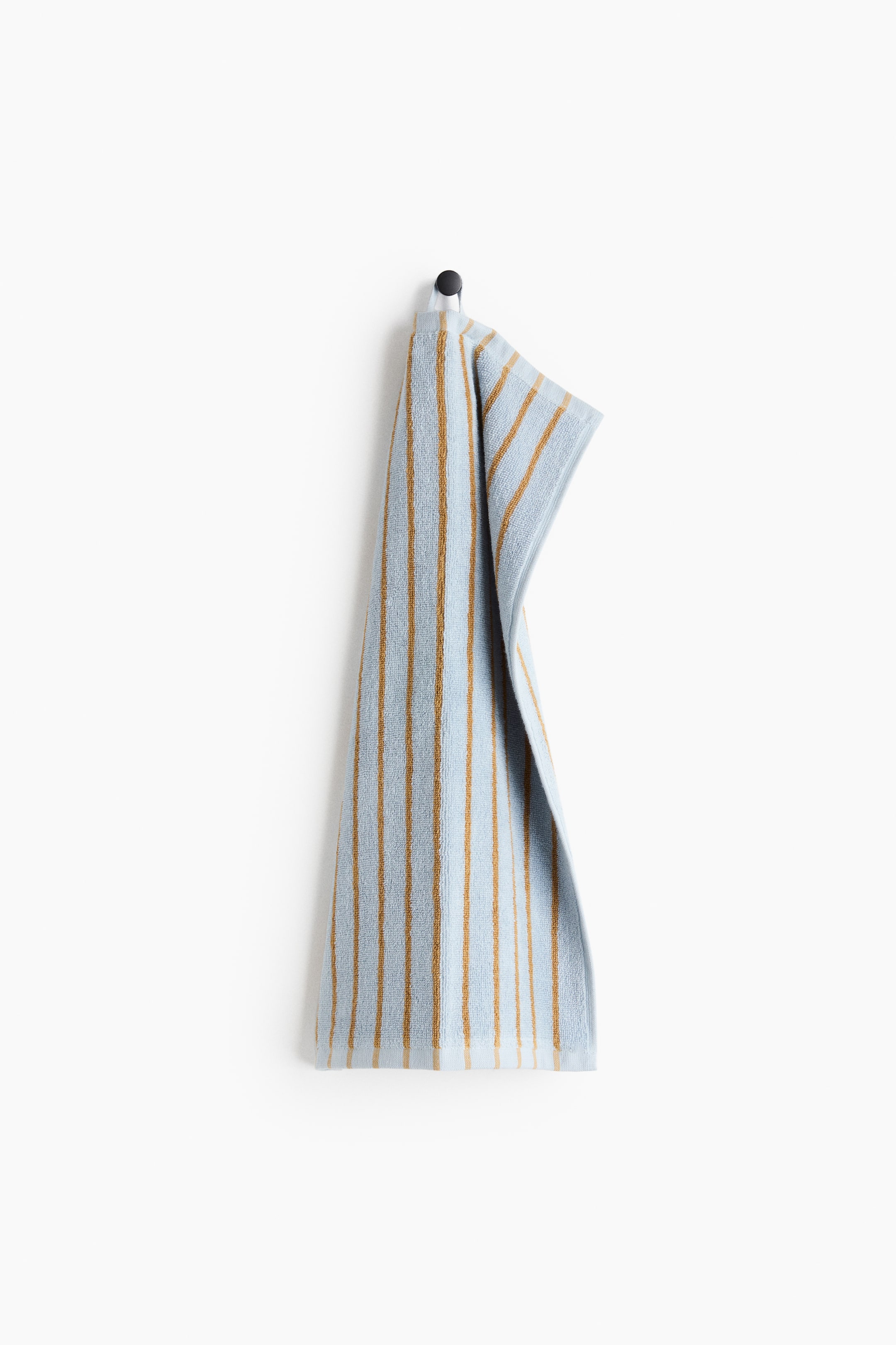 View larger image: A light blue guest towel with vertical yarn-dyed brown stripes hangs by its top loop from a black hook, shown from the front and highlighting its soft cotton terry texture.