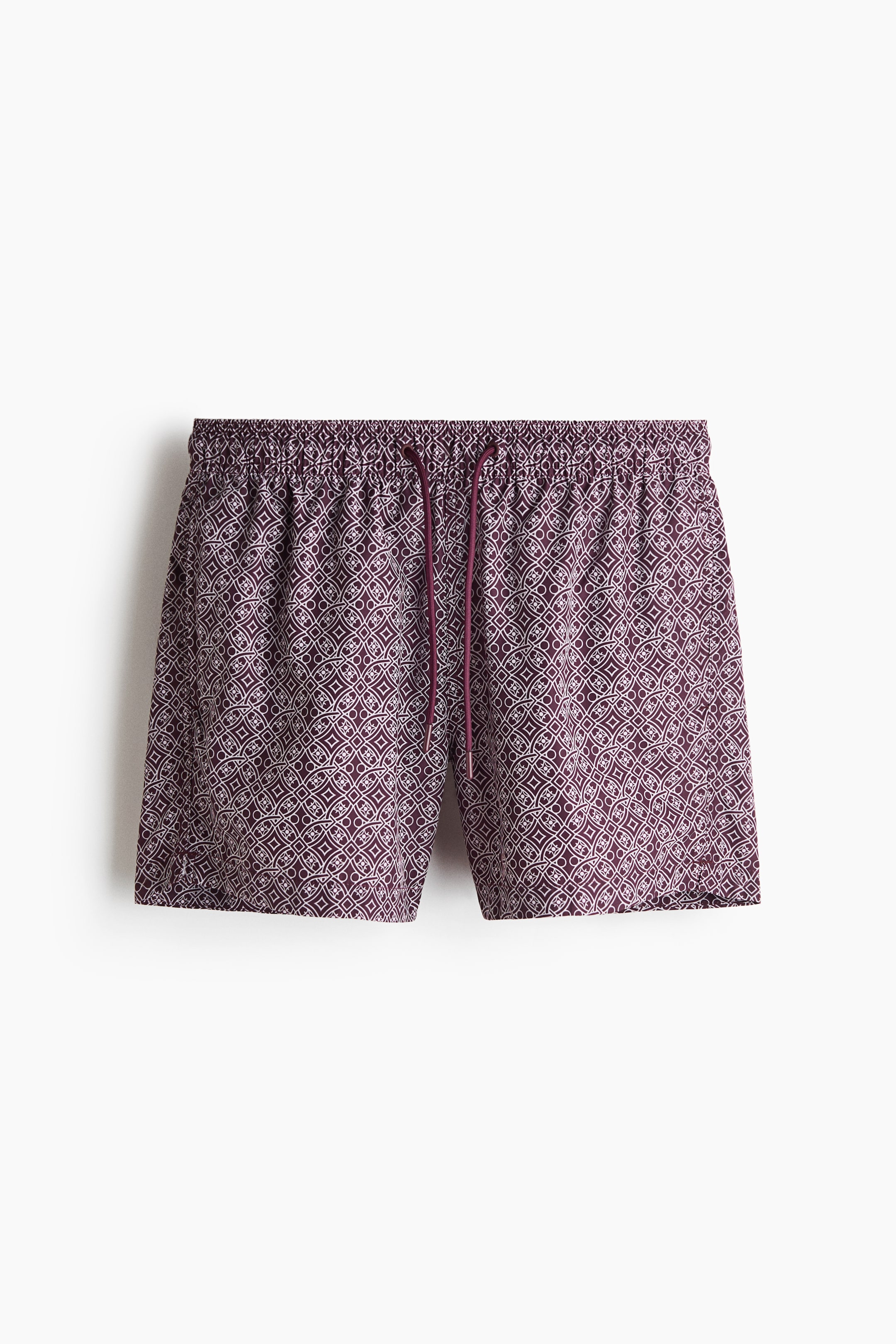View larger image: Swim shorts in a dark purple base with a light geometric pattern of interlocking circles and squares, shown from a slight front angle. They feature an elastic waistband with a matching purple drawstring and a mid-thigh length.
