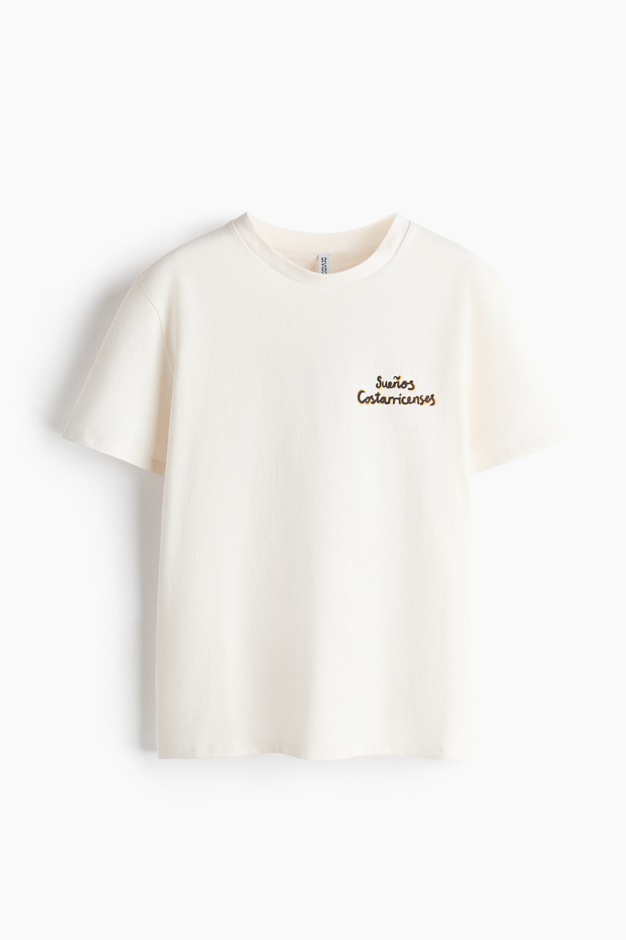Ver imagen más grande: Una camiseta color crudo con cuello redondo, mangas cortas y texto bordado en marrón que dice "Sueños Costarricenses" en la parte superior izquierda del pecho.