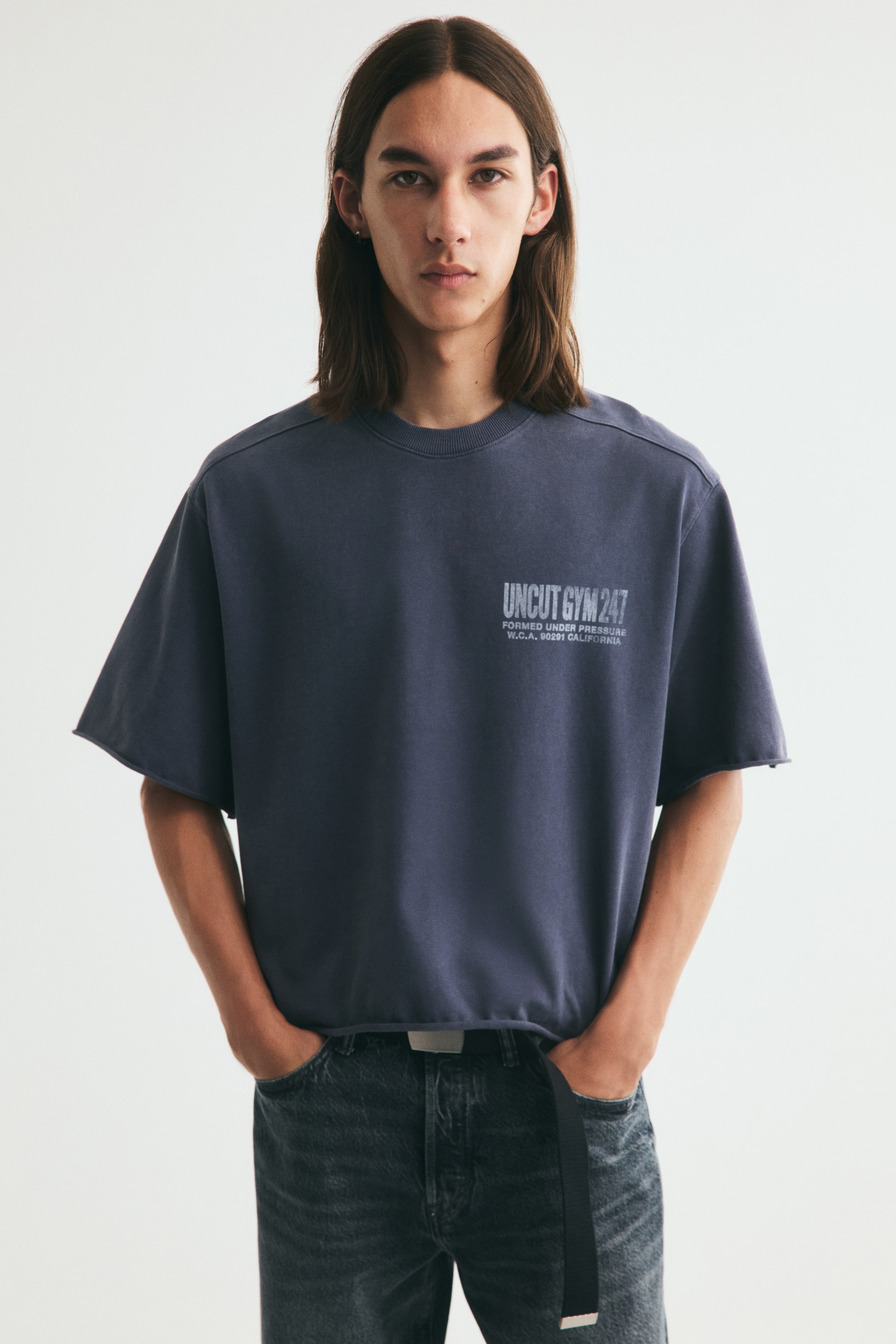 View larger image: A short, boxy-style T-shirt in heavyweight cotton jersey with a chest print, a round, rib-trimmed neckline, dropped shoulders, and roll edges at the cuffs and hem is worn by the model. The oversized fit creates a baggy, extra-loose silhouette as the model stands.