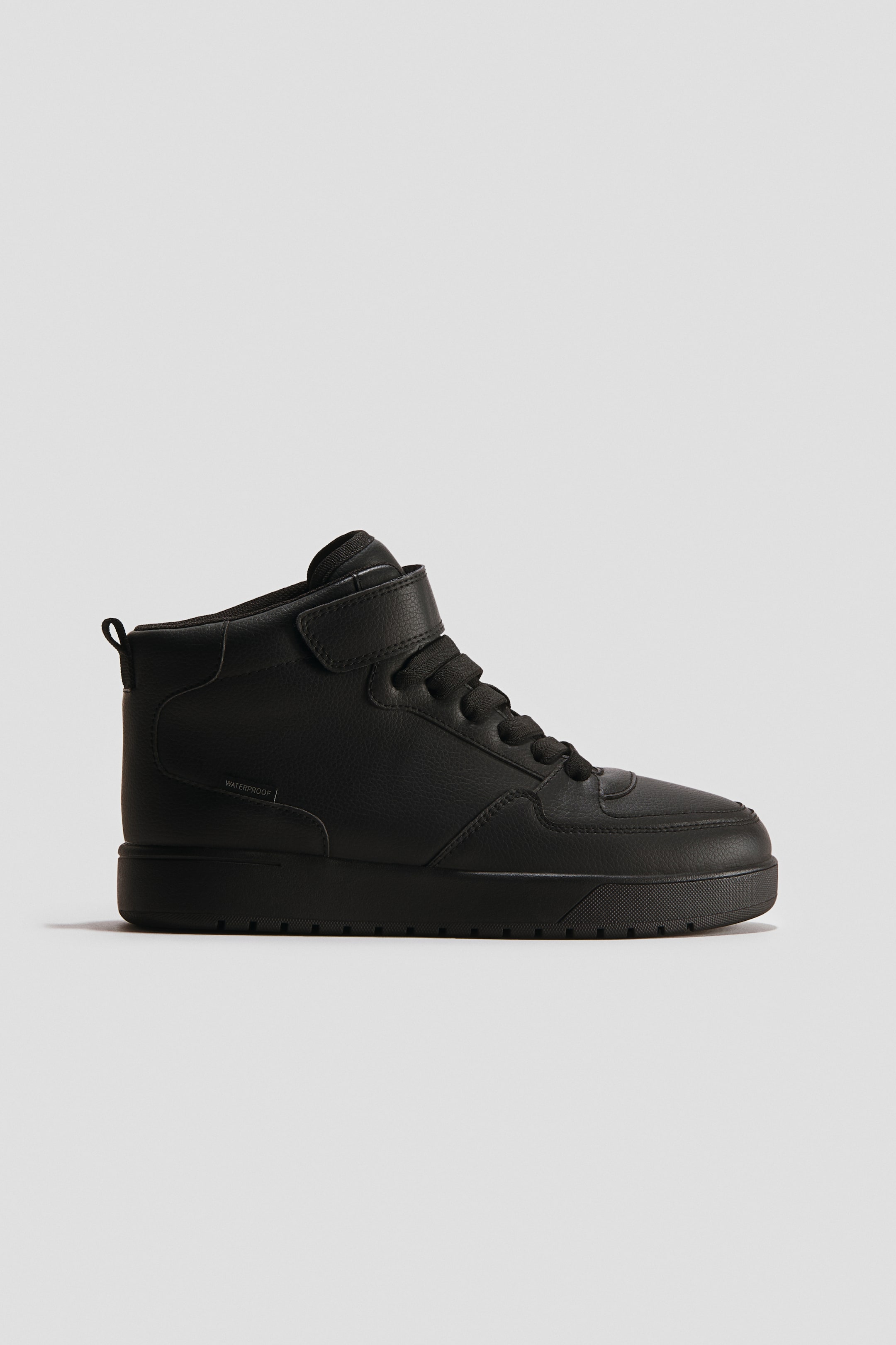 Grotere afbeelding bekijken: Een zwarte hoge sneaker is naar rechts gericht, met een gestructureerd bovenwerk, zwarte veters, een enkele klittenbandsluiting bij de enkel en een dikke zool, met "WATERPROOF" zichtbaar aan de zijkant.
