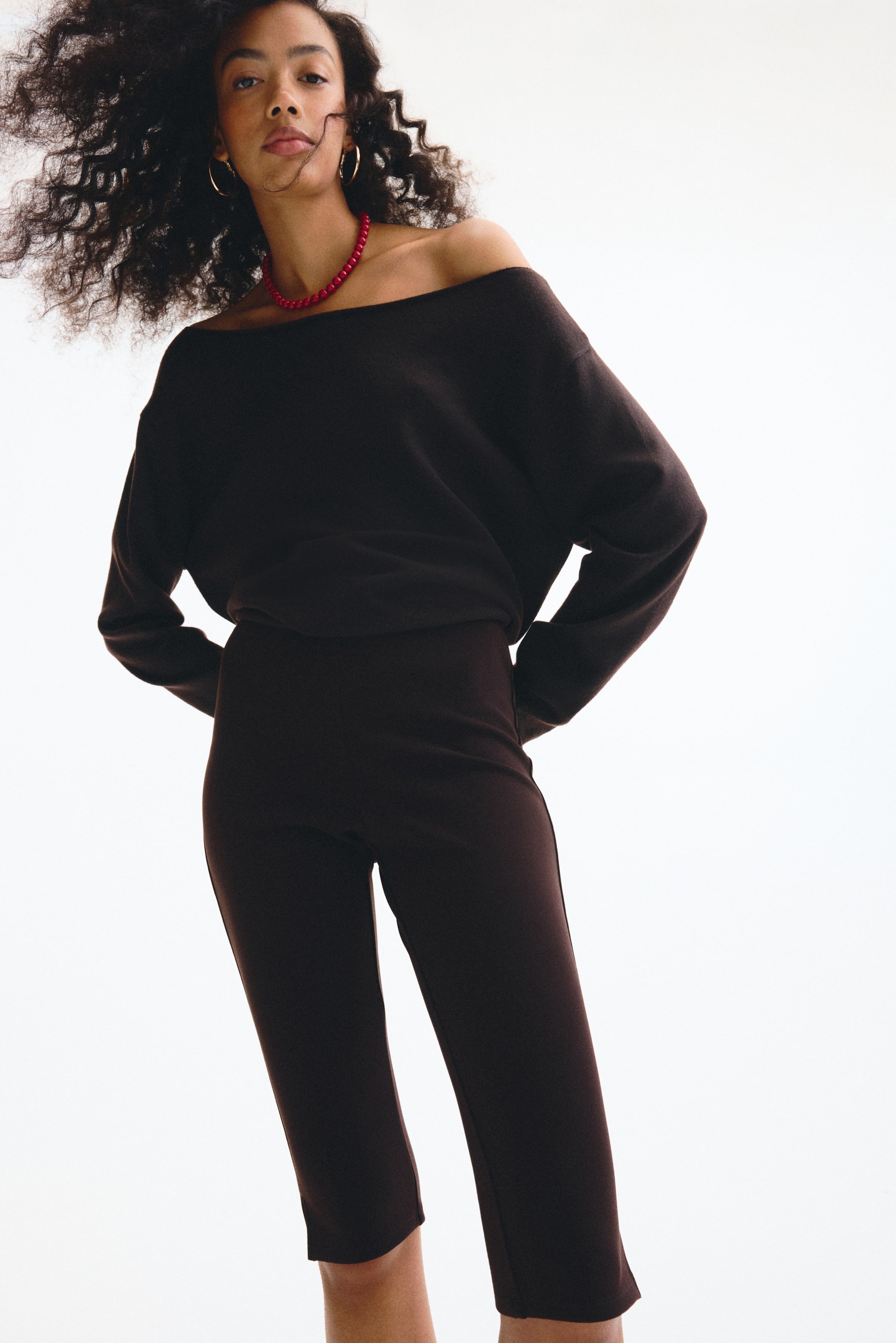 Ampliar la imagen: Pantalones oscuros ajustados de 3/4 de largo hechos de una tela de jersey suave y pesada que lleva la modelo. Los pantalones cuentan con pequeñas aberturas en los dobladillos.