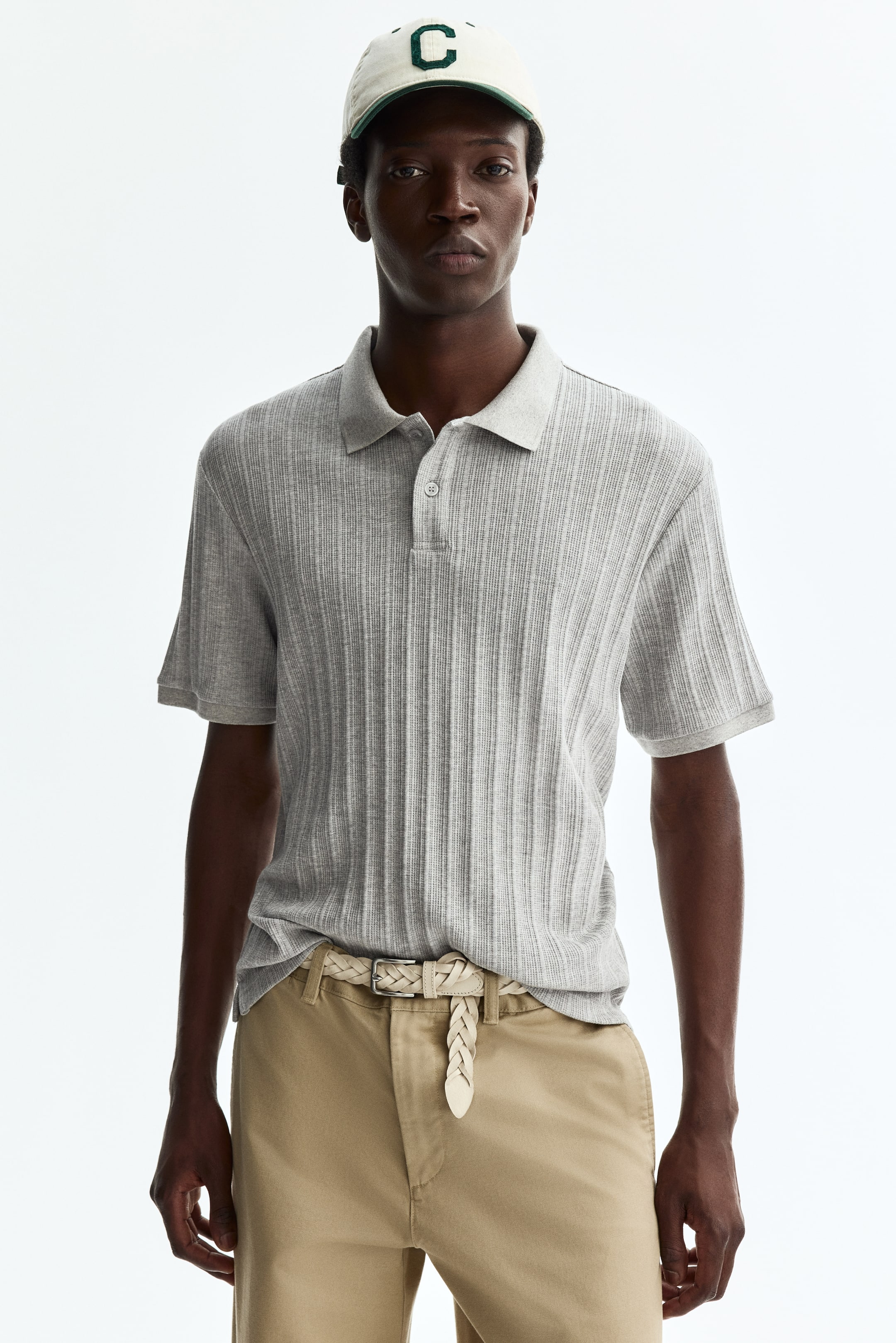 View larger image: A light grey ribbed knit polo shirt is being worn, facing forward, featuring a standard collar, a two-button placket, and short sleeves, and is appearing with a relaxed fit.
